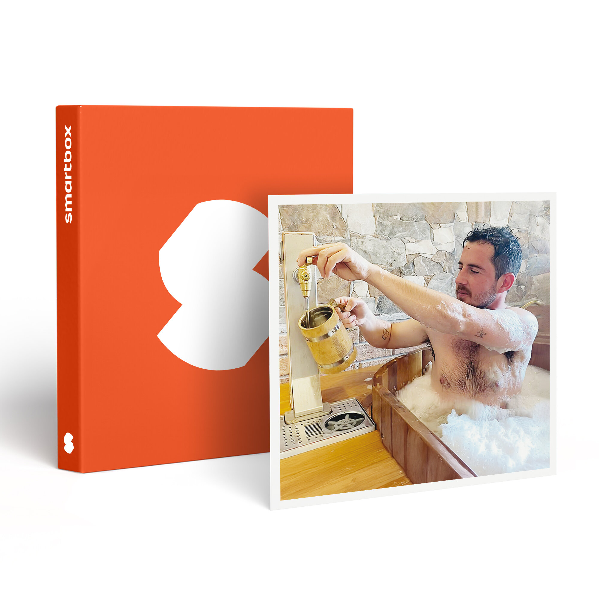 Hombre en bañera de madera con espuma, llenando un vaso de madera de un grifo. Caja naranja con logo blanco en el fondo.