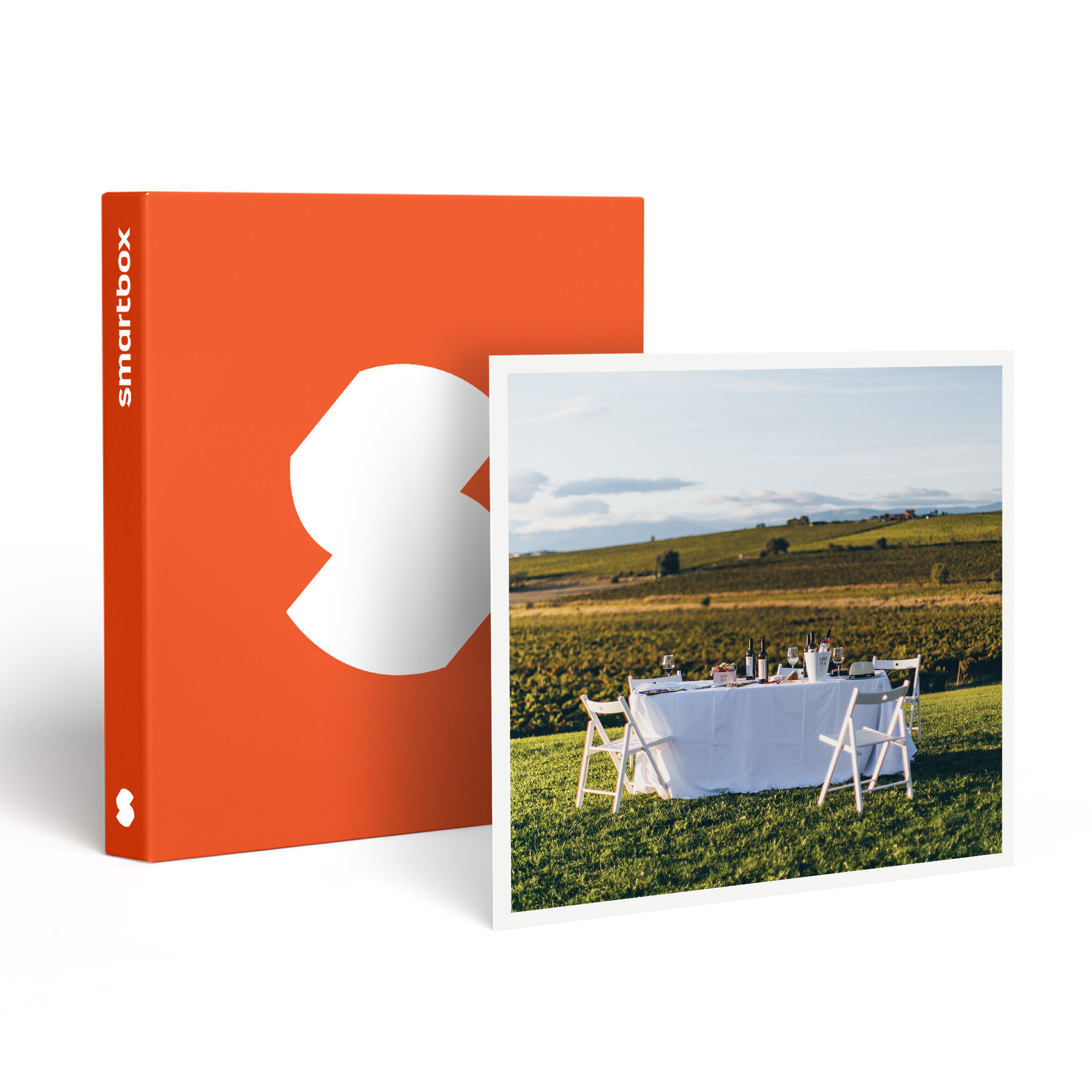 Una caja naranja de Smartbox junto a una imagen enmarcada de una mesa preparada para una comida en un viñedo.
