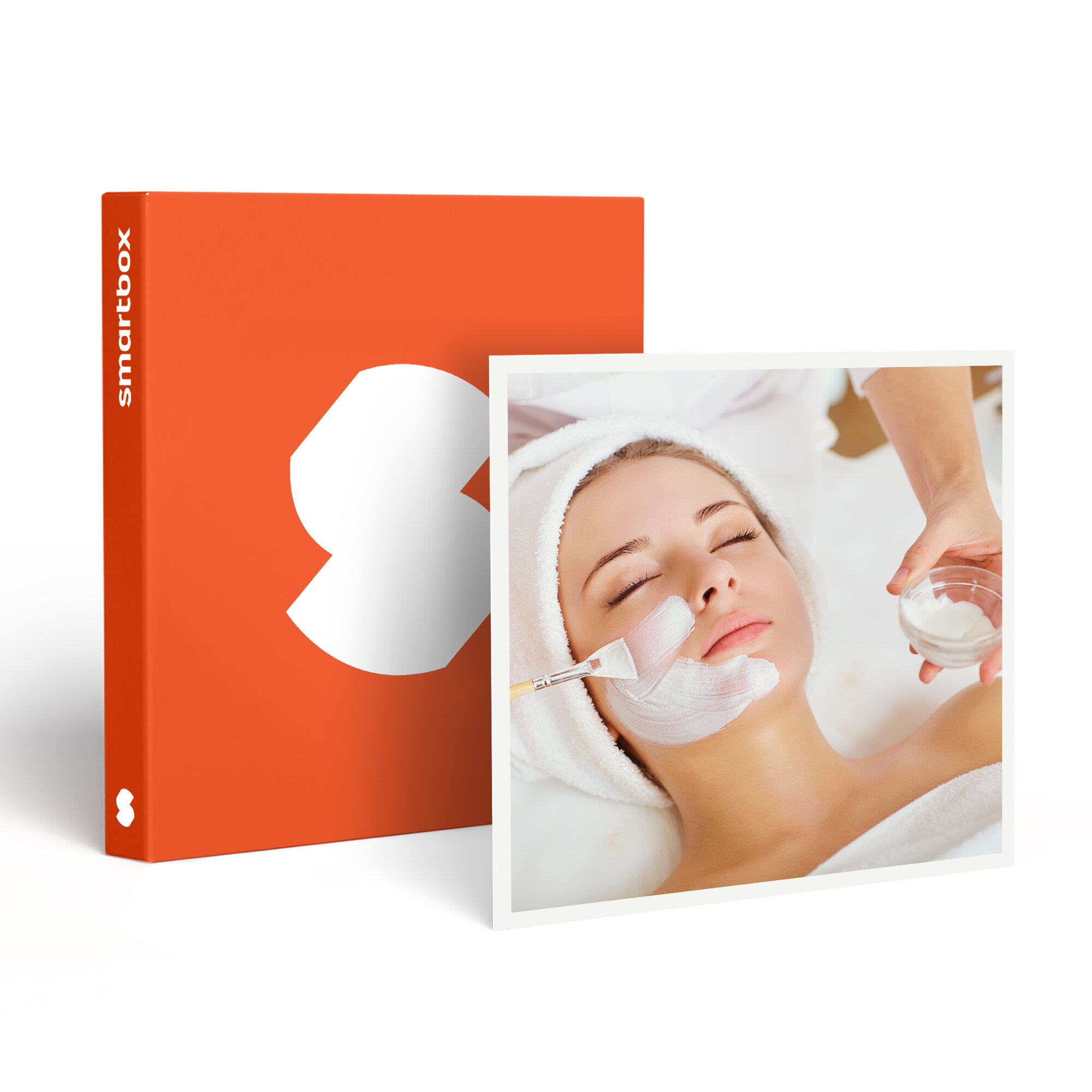 Una mujer recibe un tratamiento facial. Se le aplica una mascarilla en la cara con un pincel. Hay una caja naranja en el fondo.