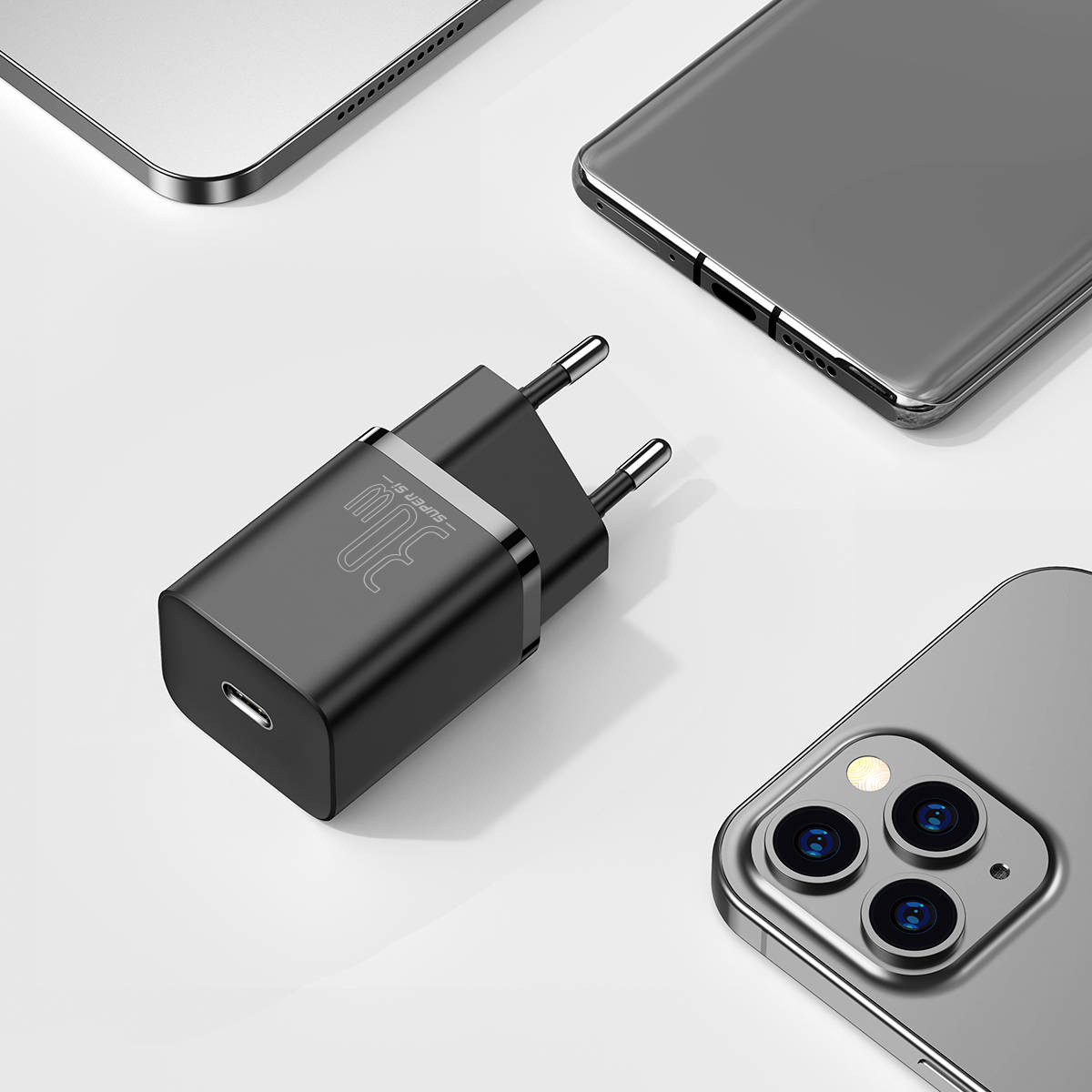 Schwarzes 30-W-Ladegerät mit silbernen Stiften, umgeben von einem Laptop und drei Smartphones.