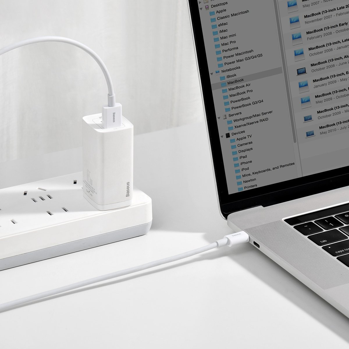 Een witte oplader aangesloten op een stopcontact, verbonden met een laptop met een witte kabel. De laptop staat open.