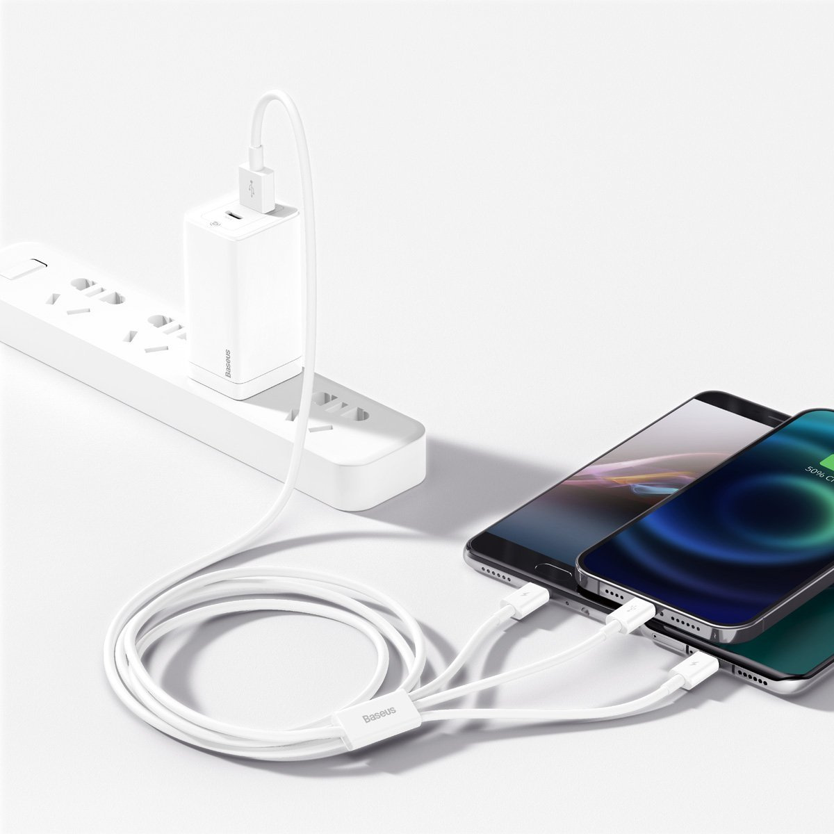 Witte oplader en kabel die drie smartphones opladen. Oplader is aangesloten op een witte stekkerdoos. Telefoons zijn zwart en groen.