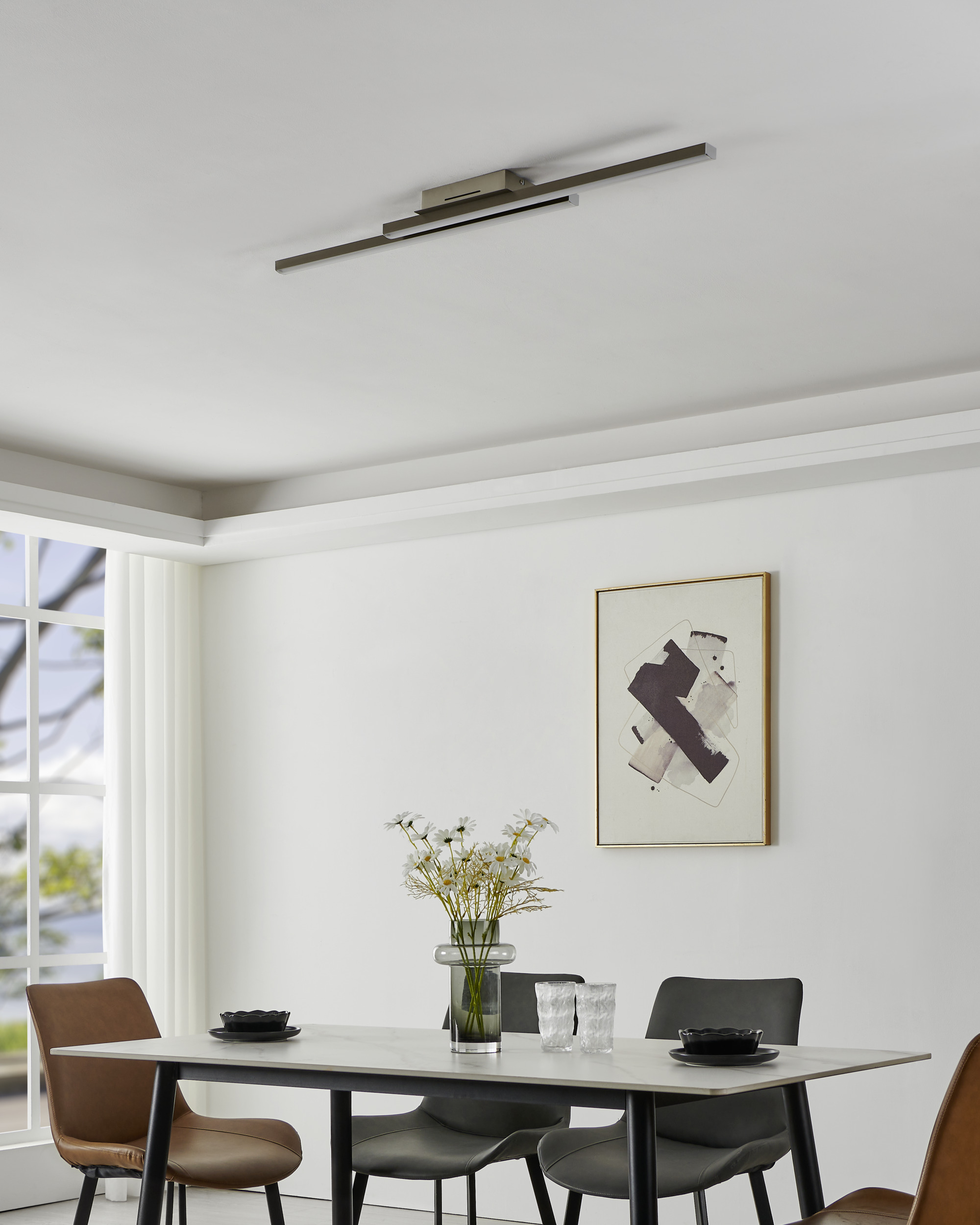 Ein Esszimmer mit Tisch, Stühlen, Blumen, Kunst und einer Deckenleuchte. Weiße Wände und ein Fenster.