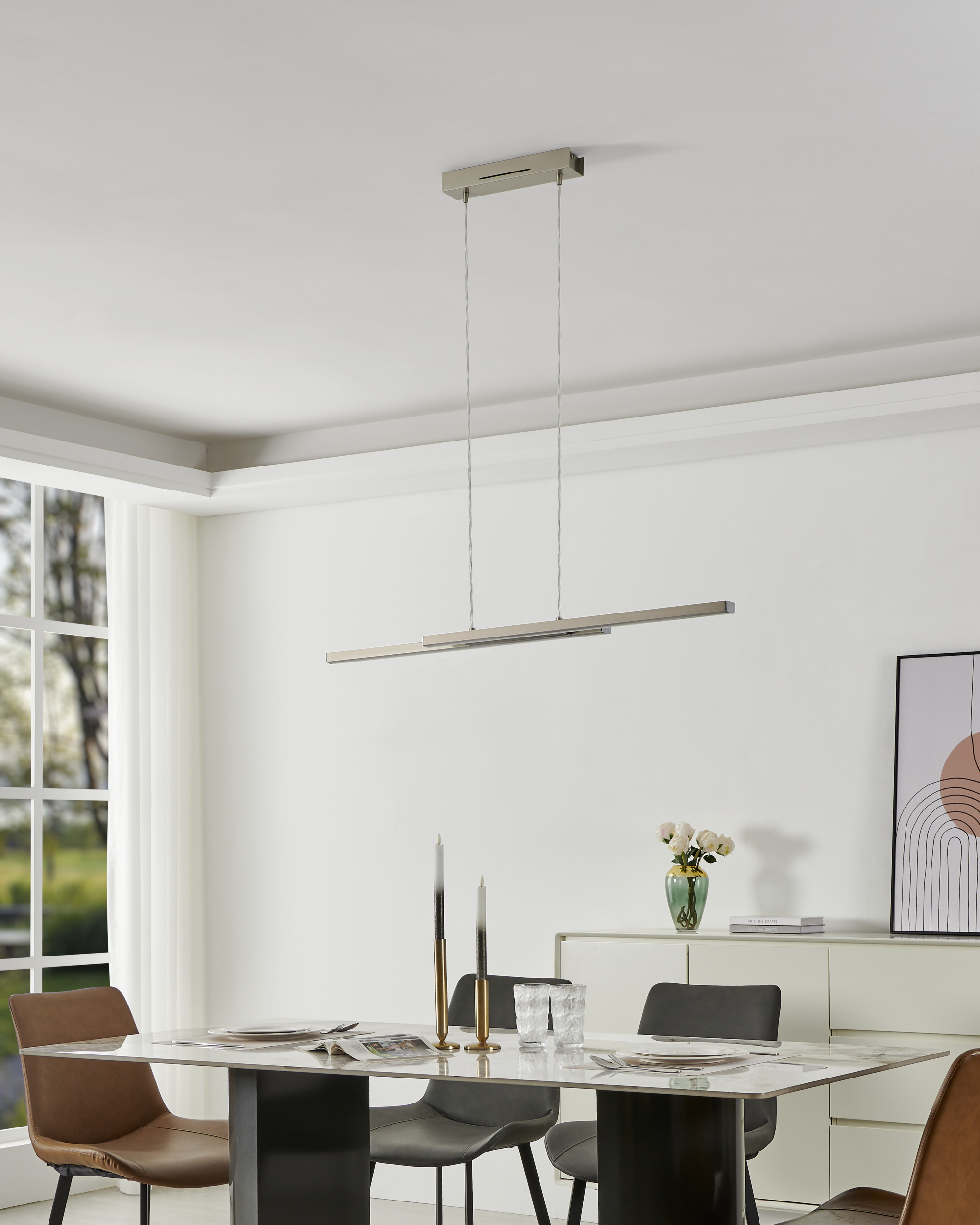 Ein Esszimmer mit Tisch, Stühlen, Kronleuchter und Sideboard. Kerzen und Blumen stehen auf dem Tisch.