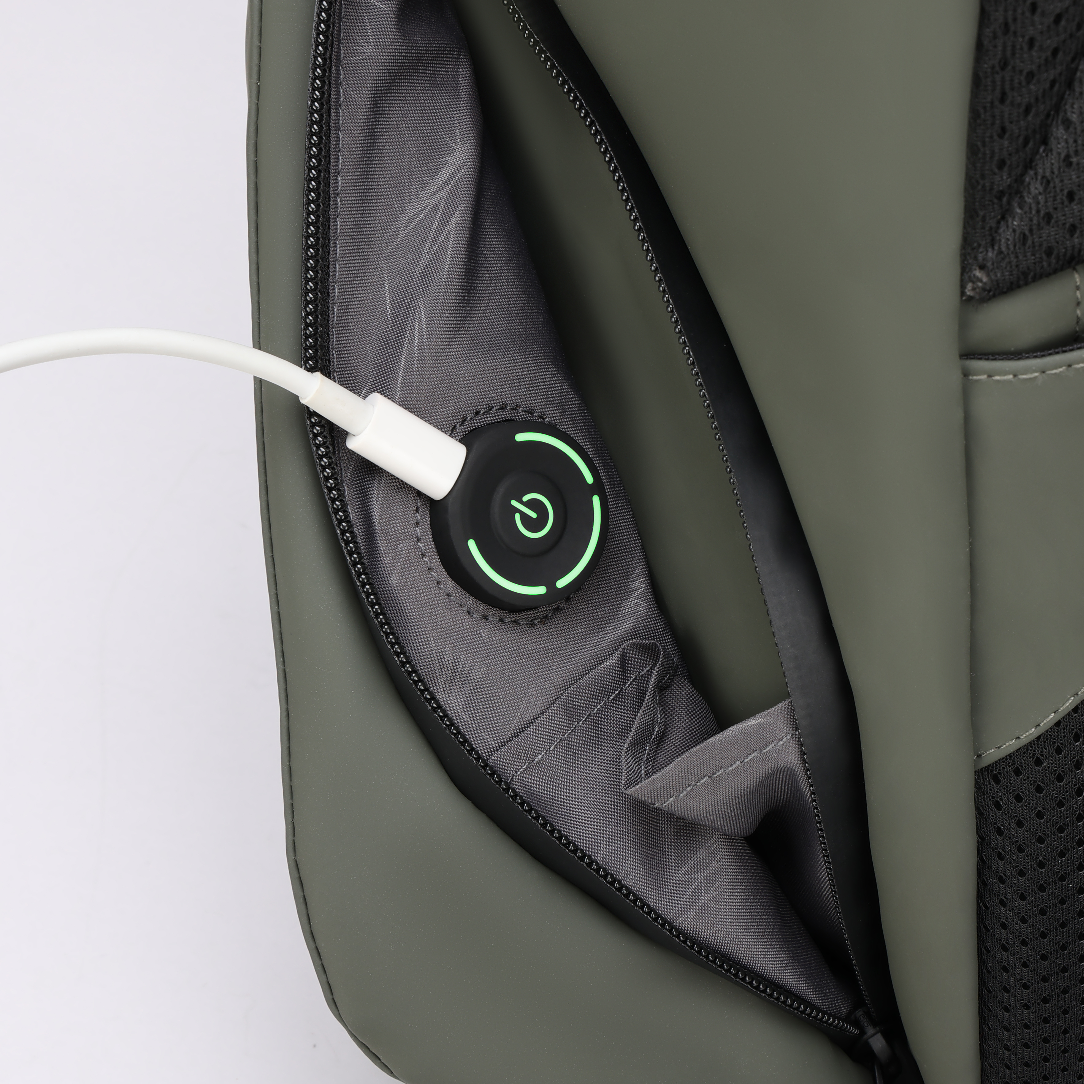 Primo piano di uno zaino con una porta di ricarica e un cavo bianco collegato. Il pulsante di accensione si illumina di verde.