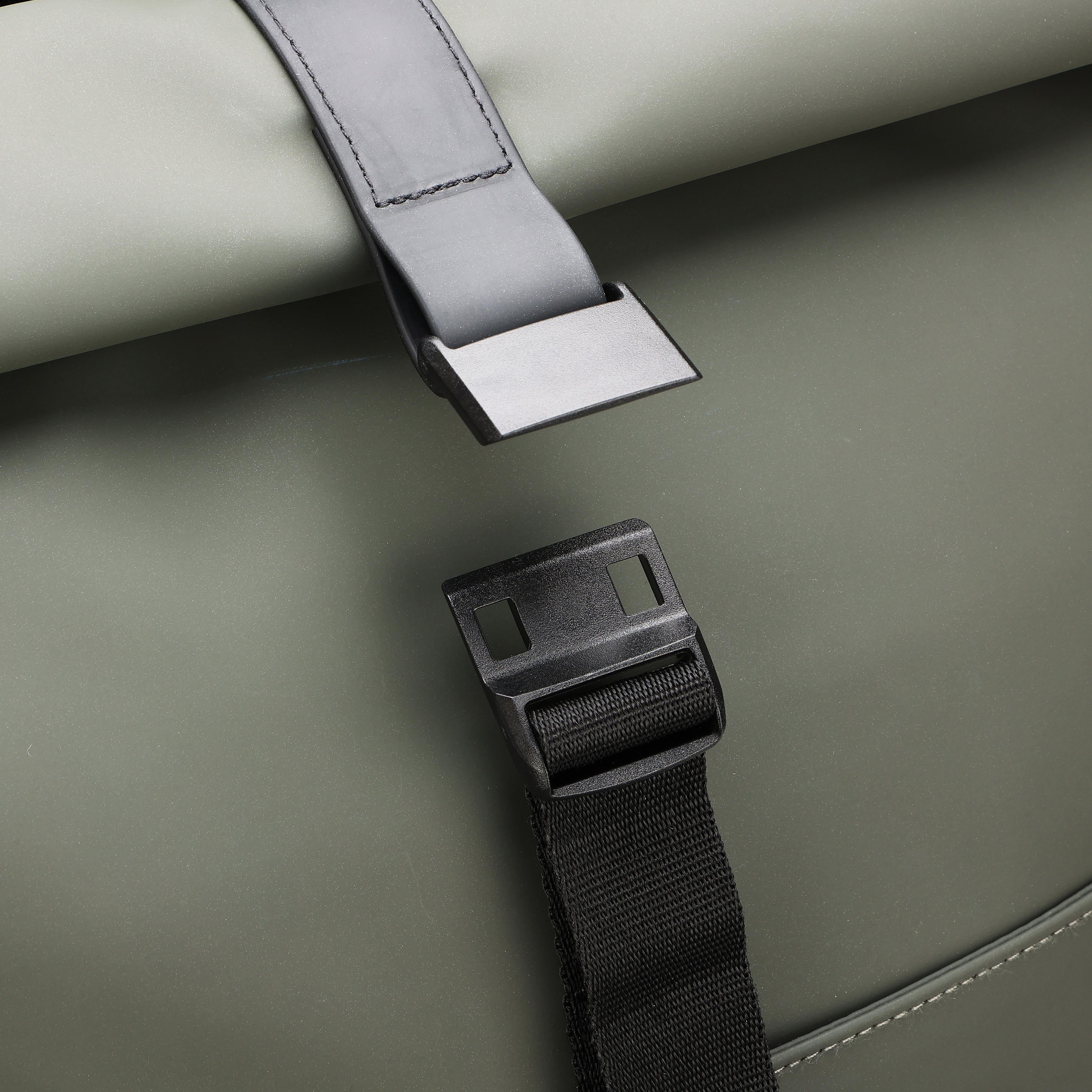 Primo piano di una chiusura di borsa. Fibbia di plastica nera su cinturino nero su sfondo verde.