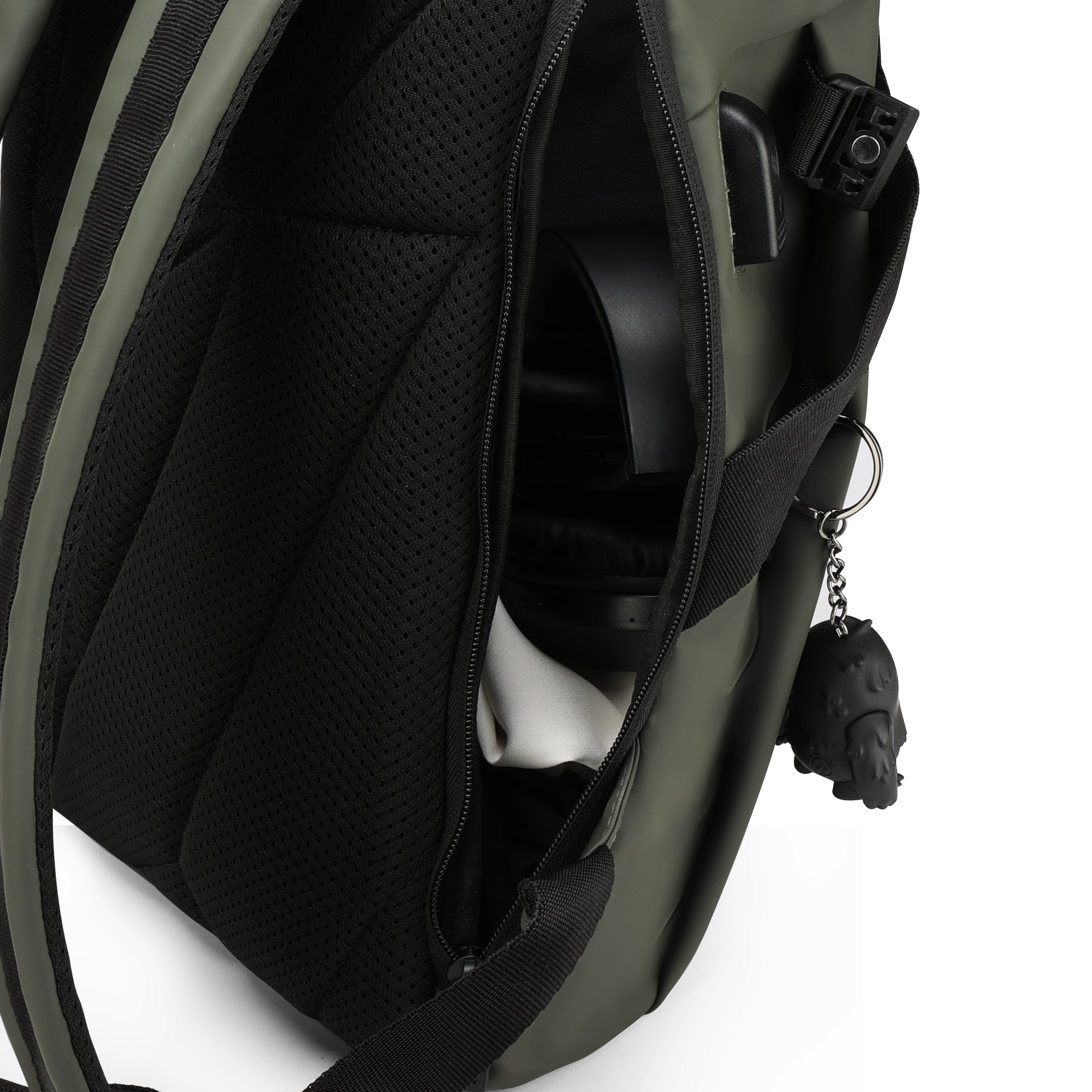 Dettaglio dello zaino verde. Cerniera aperta rivela cuffie e tessuto bianco. Cinturino nero e portachiavi con figura nera.