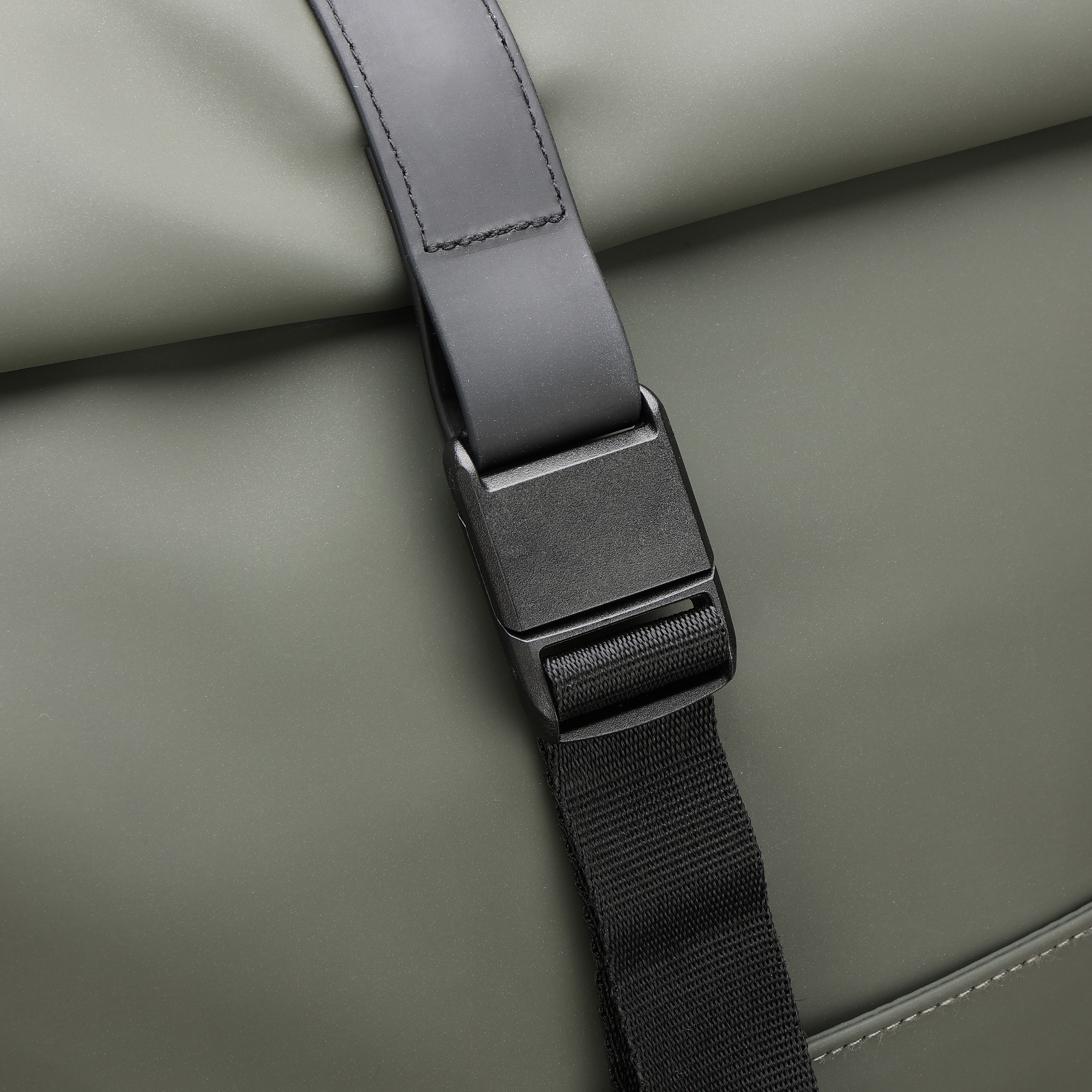 Primo piano di una borsa. Cinturino nero con fibbia. La borsa è verde oliva.