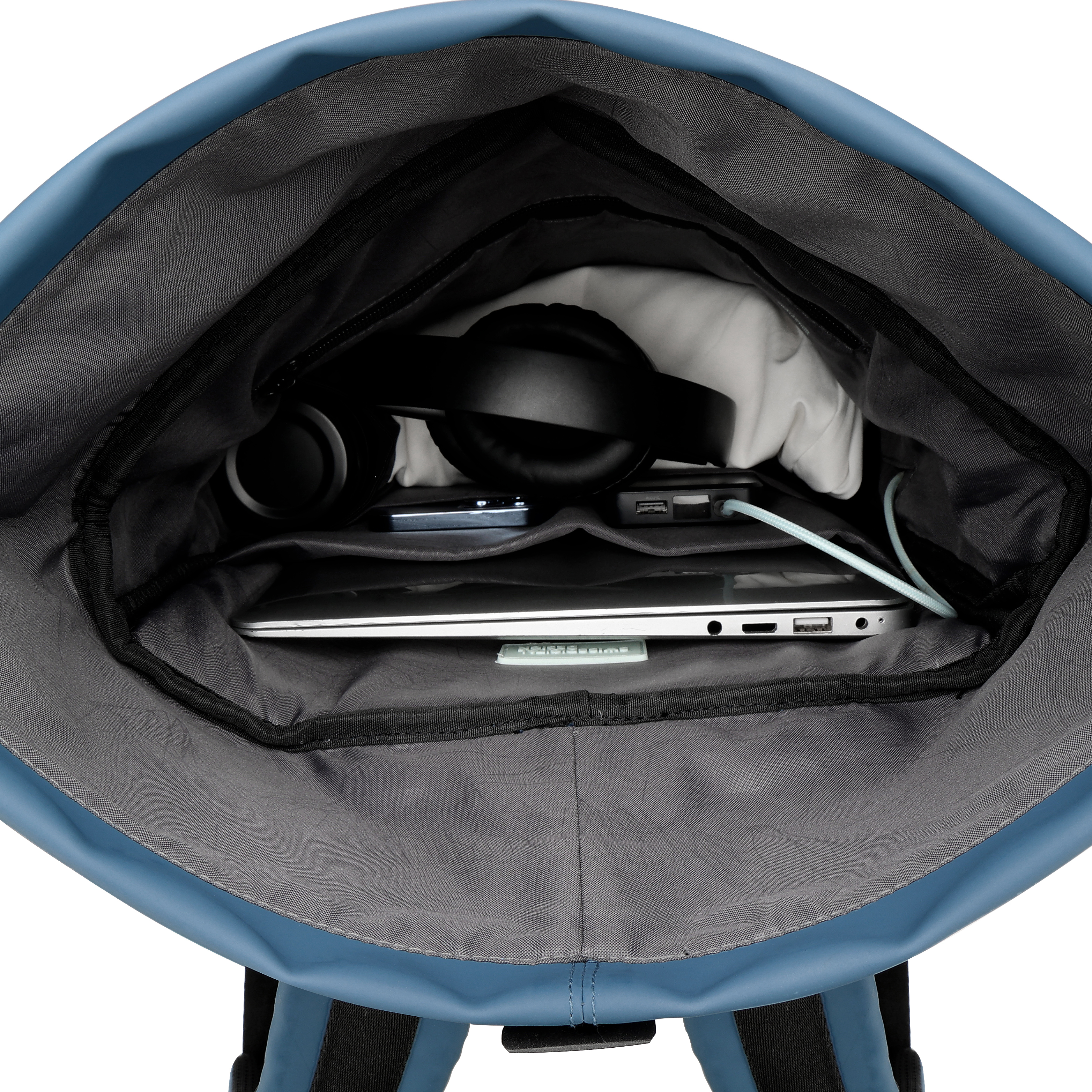 Zaino blu aperto rivela laptop, cuffie, telefono, caricatore e altri oggetti. Lo zaino è su sfondo bianco.