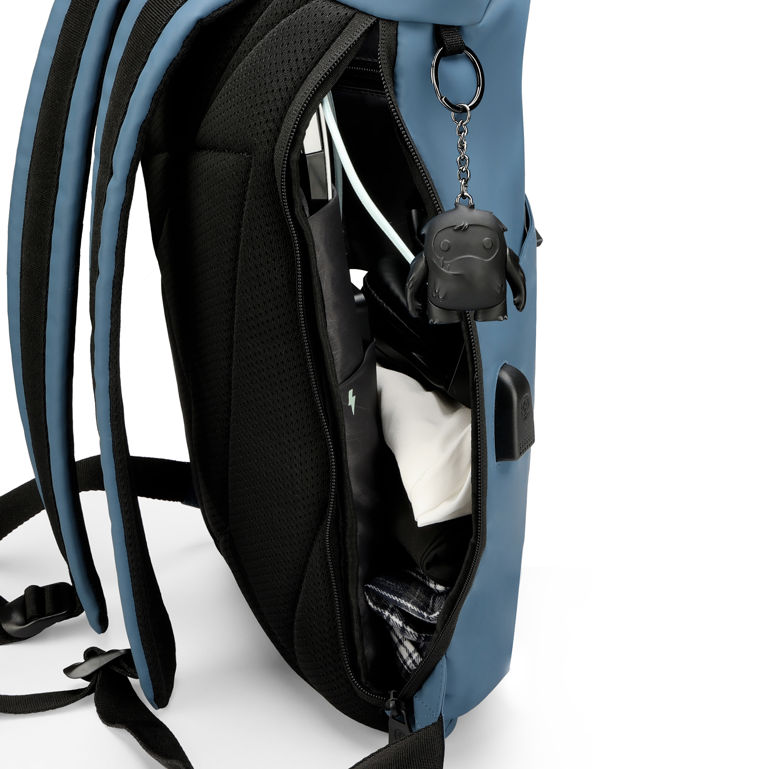 Zaino blu aperto, rivela il contenuto: vestiti, portachiavi nero. Sfondo bianco.