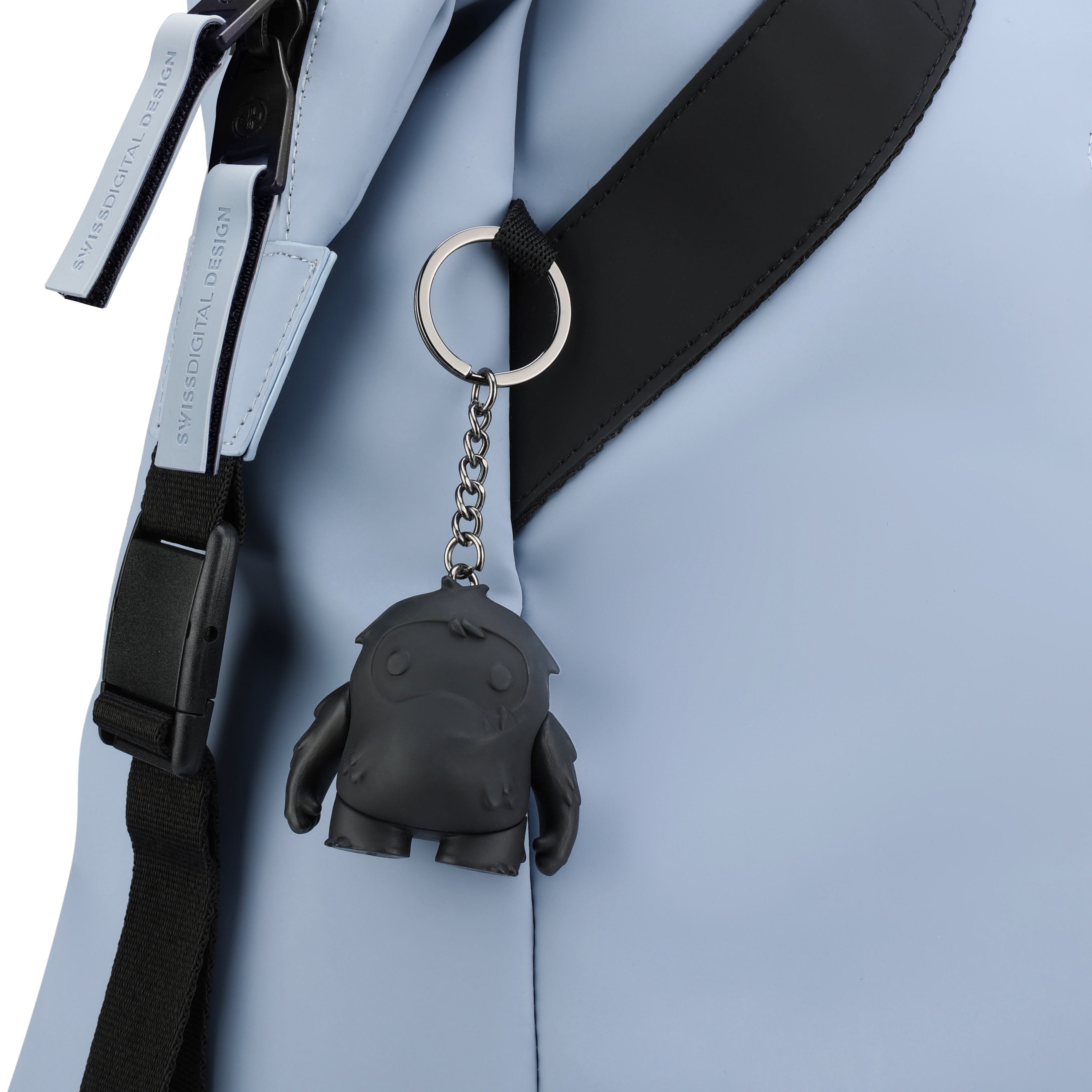 Un primo piano di una borsa blu con cinturino nero e un portachiavi nero. Il portachiavi è un mostro grigio scuro.