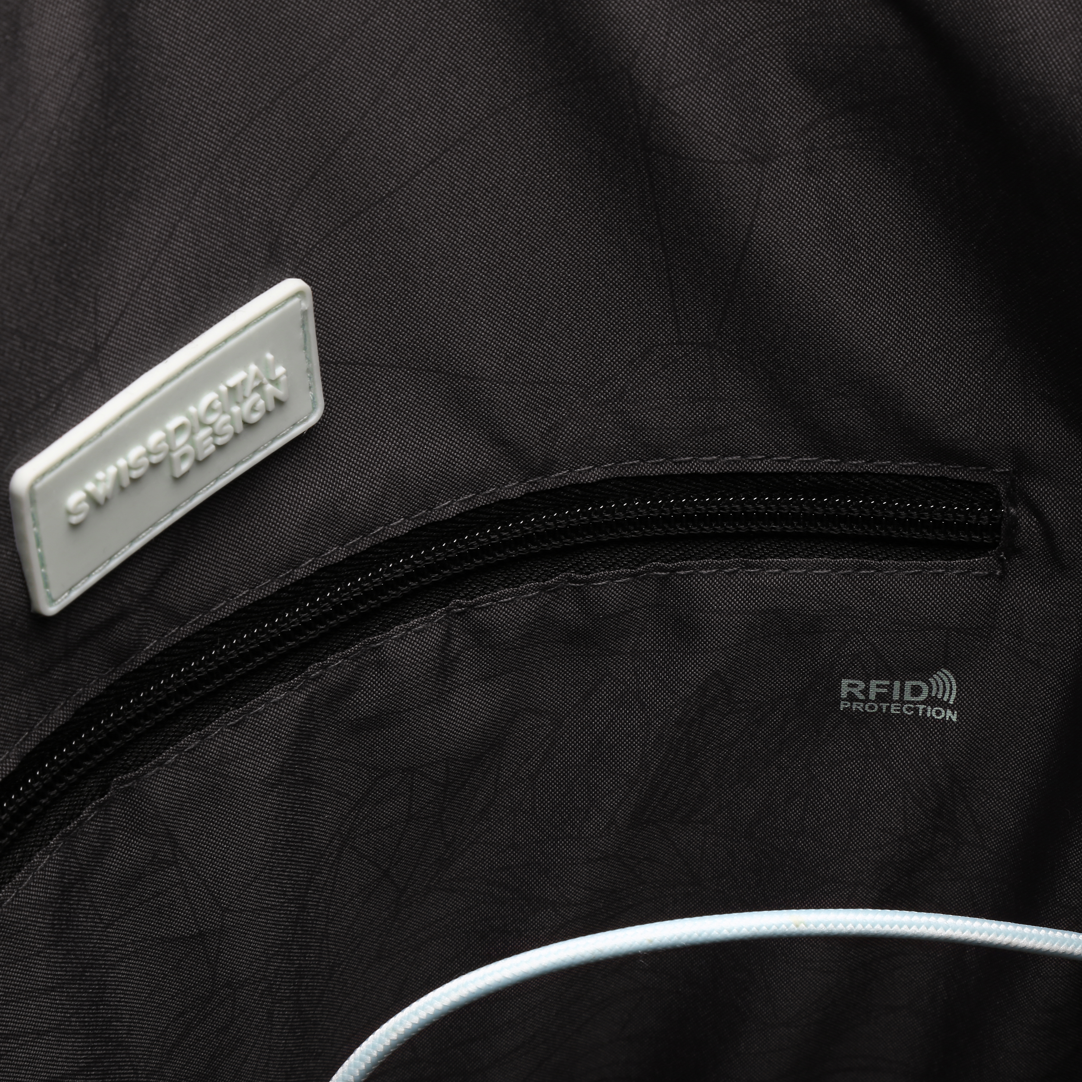 Primo piano di una borsa nera con cerniera, etichetta Swissdigital Design ed etichetta di protezione RFID.