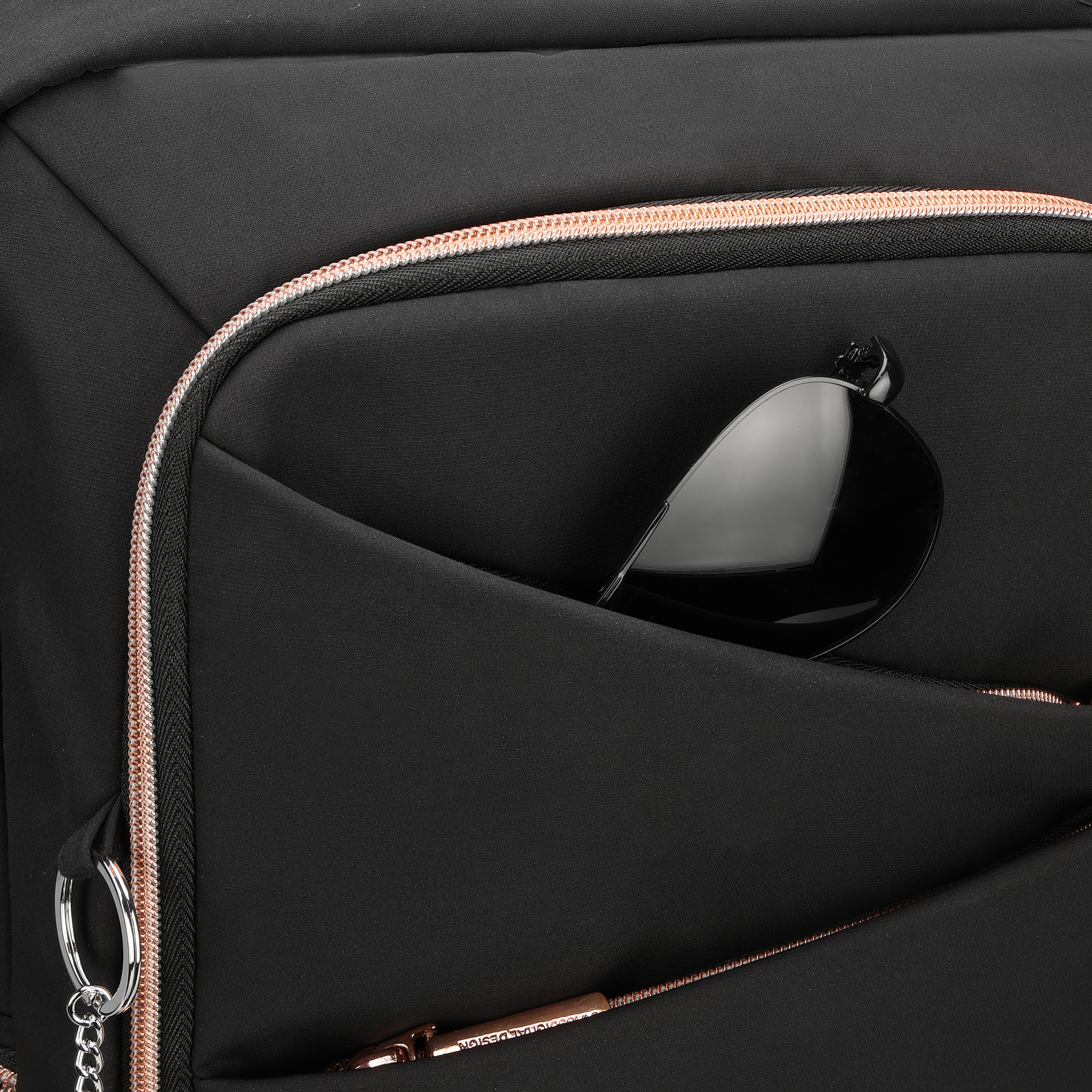 Primo piano di uno zaino nero con una tasca che contiene occhiali da sole. Dettagli con cerniera e finiture oro rosa.