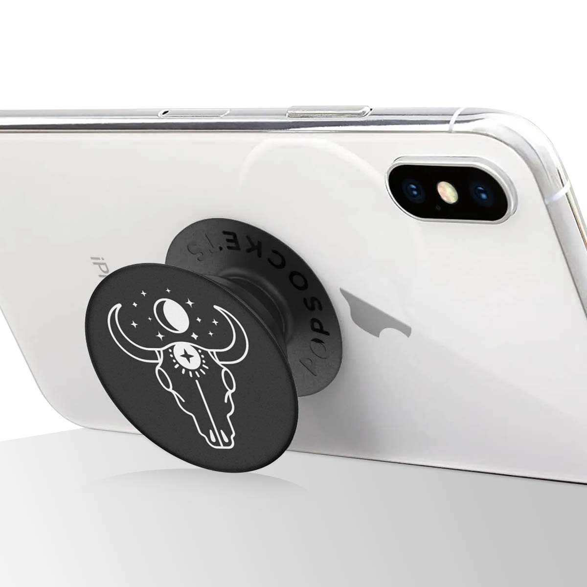 Ein weißes iPhone hat einen schwarzen PopSocket mit einem Bullenschädel-Design. Das Telefon liegt auf einer weißen Oberfläche.