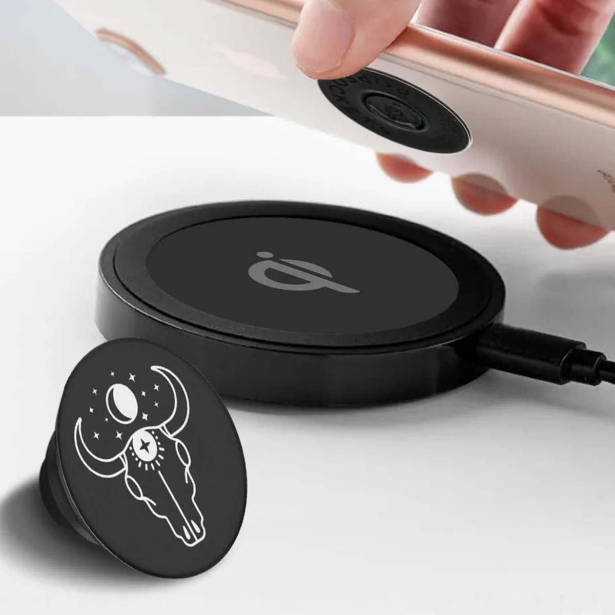 Ein Telefon wird auf ein kabelloses Ladegerät gelegt. Ein schwarzer PopSocket mit einem Bullenschädel-Design liegt daneben.