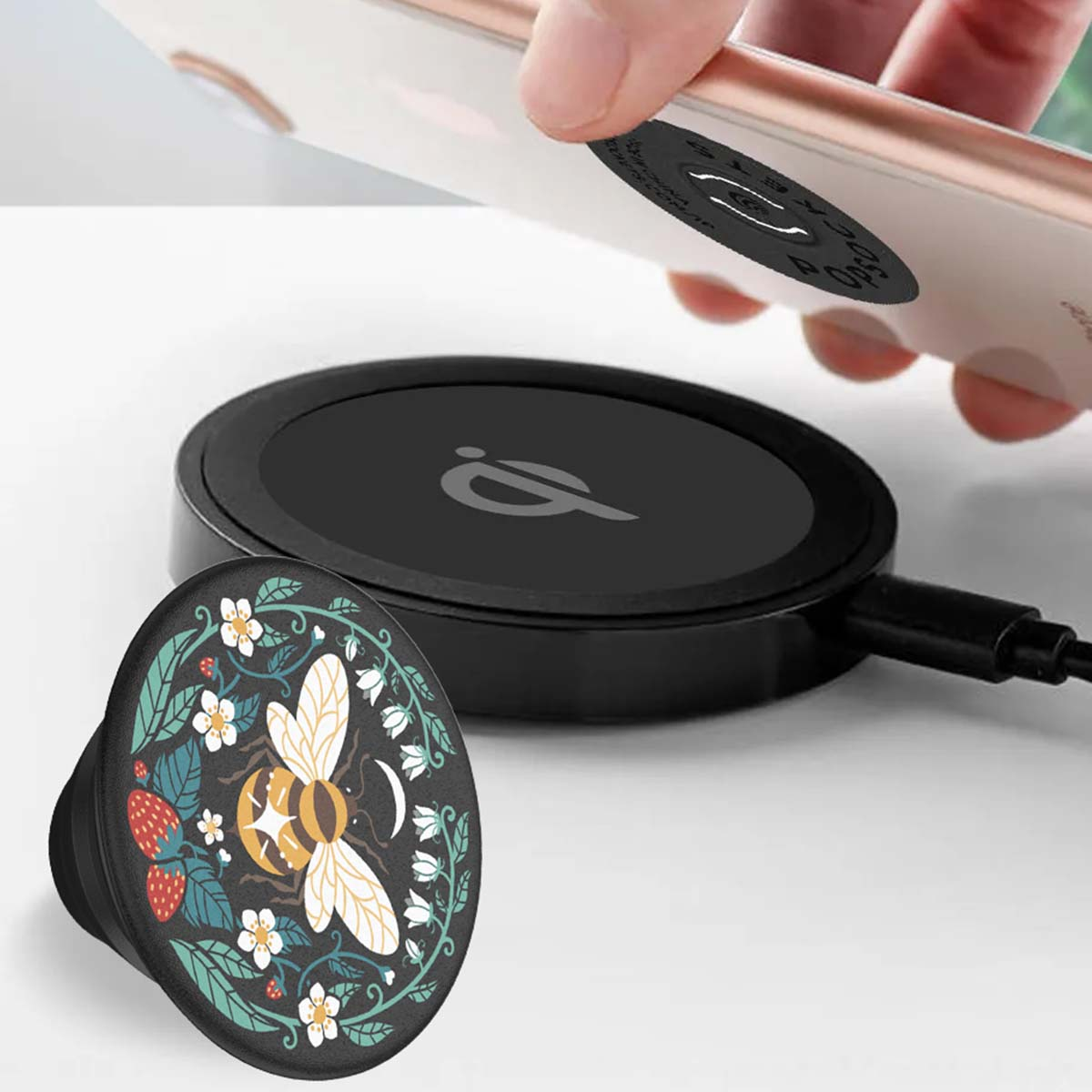 Ein Telefon wird auf ein kabelloses Ladegerät gelegt. Ein PopSocket mit Bienenmuster befindet sich im Vordergrund. Das Ladegerät ist schwarz.