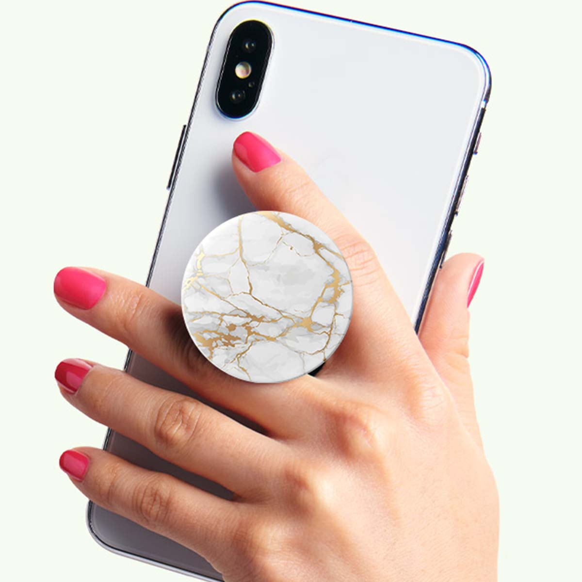 Una mano sosteniendo un teléfono blanco. Hay un pop socket con patrón de mármol. Las uñas están pintadas de rosa.