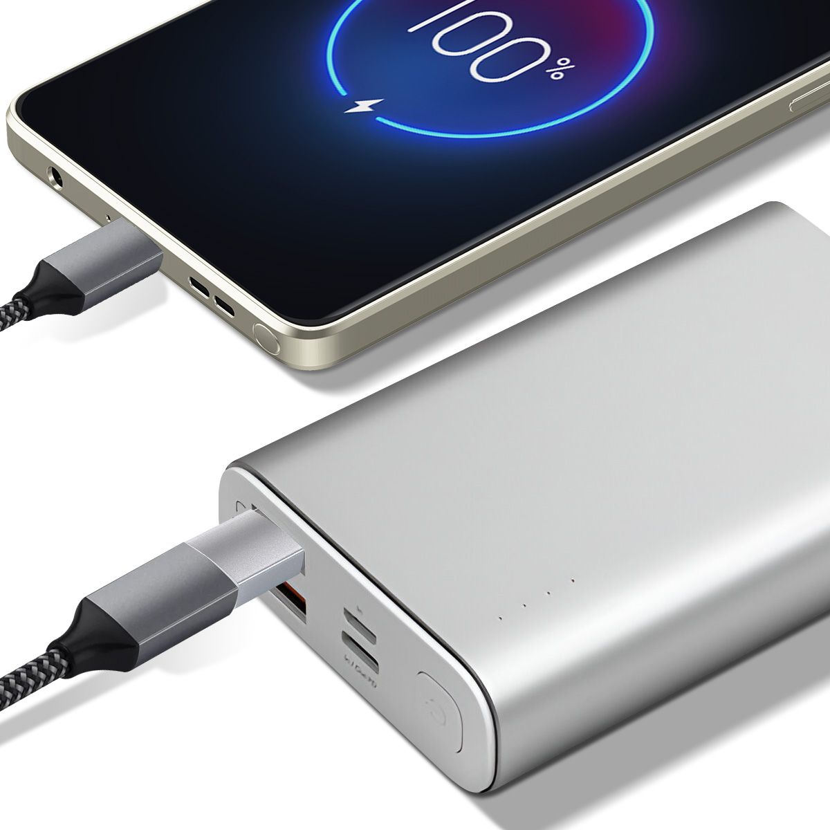 Telefon ładuje się, wyświetlając 100%. Podłączony do srebrnego power banku kablem USB-C. Power bank posiada porty ładowania.