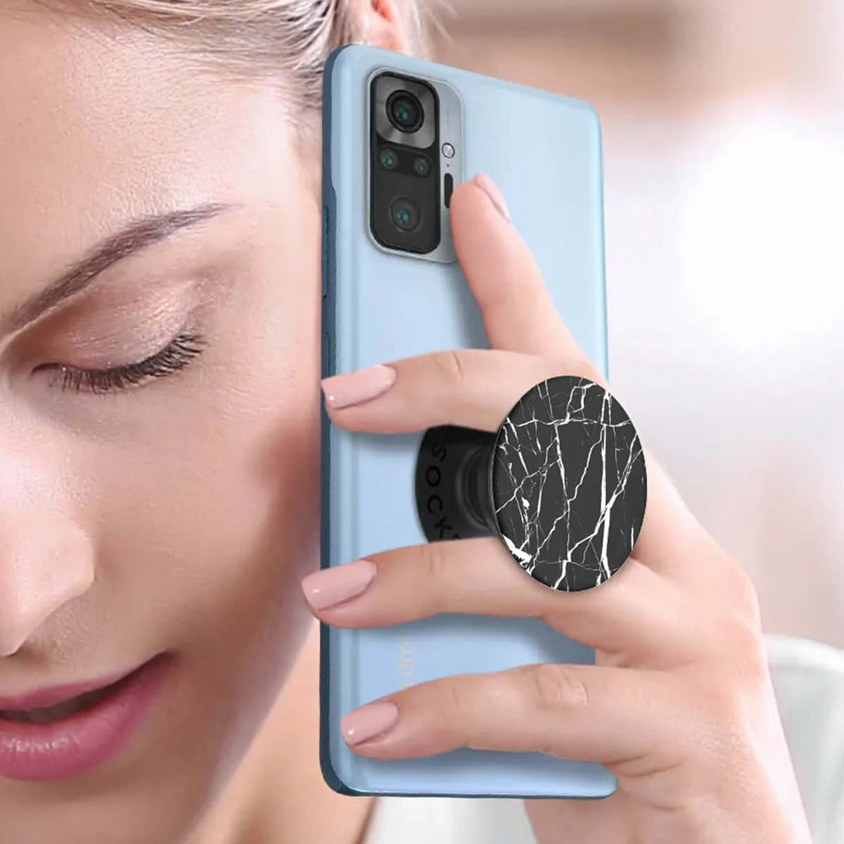 Una donna tiene in mano un telefono azzurro con un PopSocket in marmo bianco e nero. Le sue unghie sono dipinte di rosa.