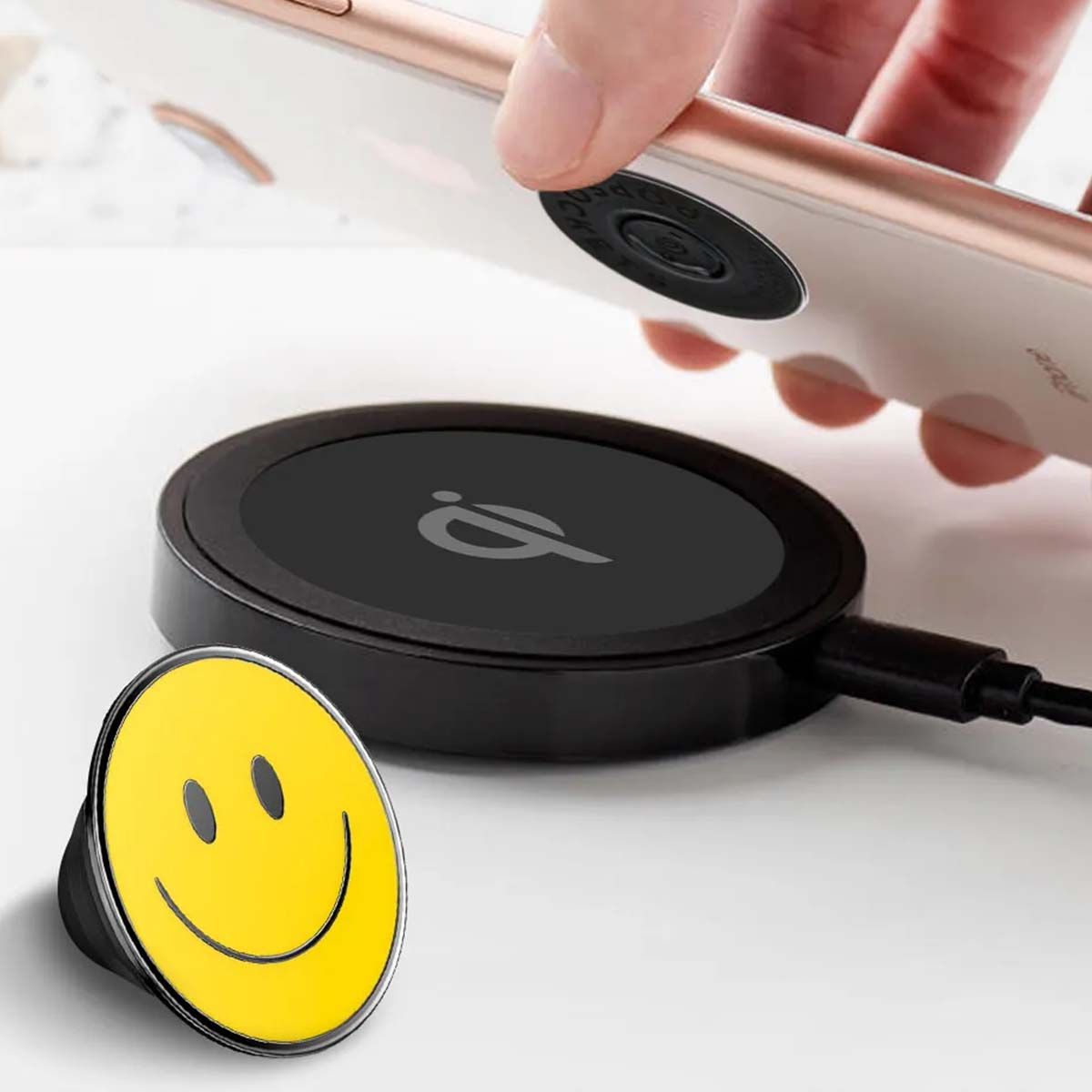 Un telefono viene posizionato su un caricatore wireless. Un PopSocket con faccina gialla è vicino. Caricatore e cavo neri visibili.