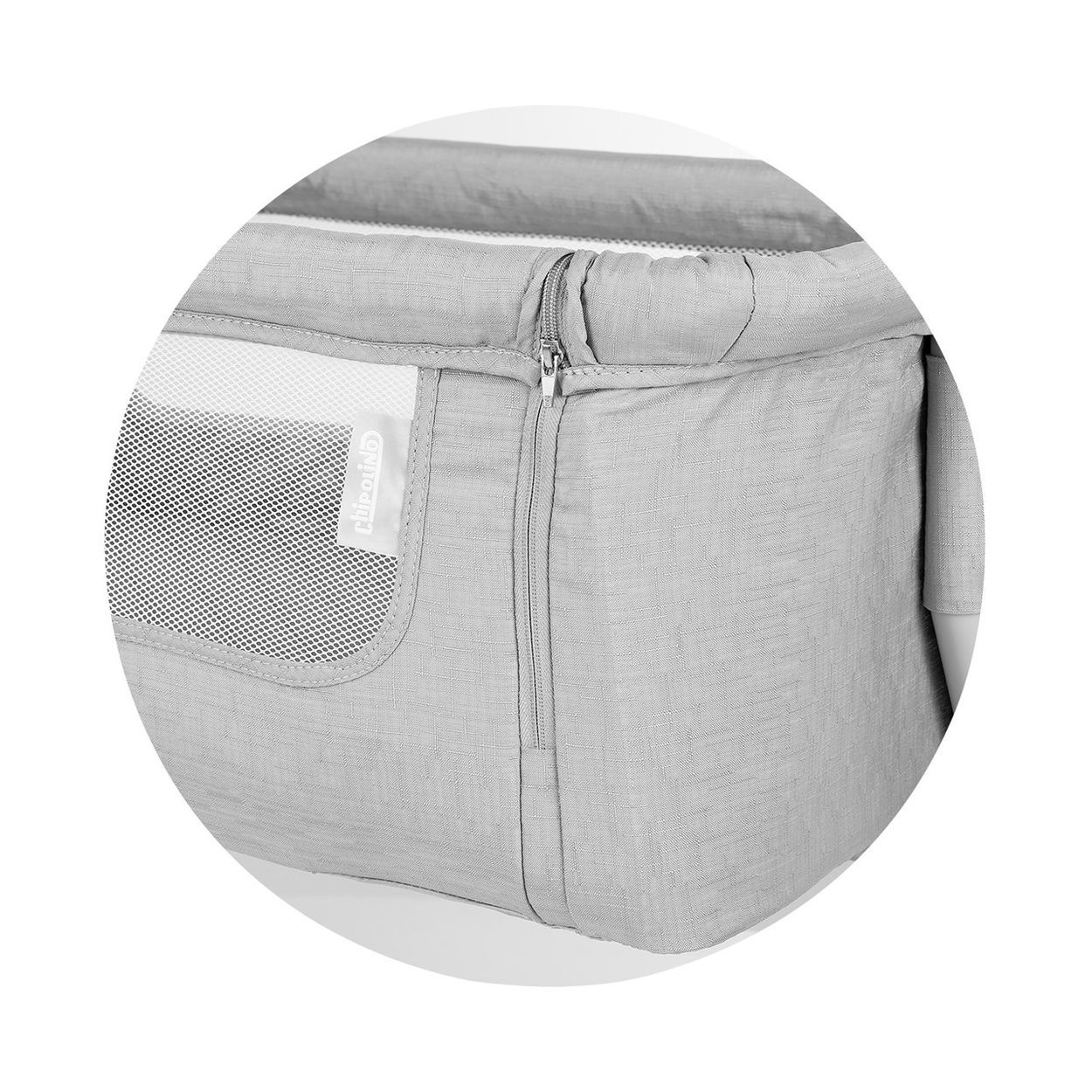 Nahaufnahme eines grauen Babybettes. Mit einem Seitenteil aus Mesh, einem Reißverschluss und einem Markenetikett. Der Stoff wirkt strukturiert.