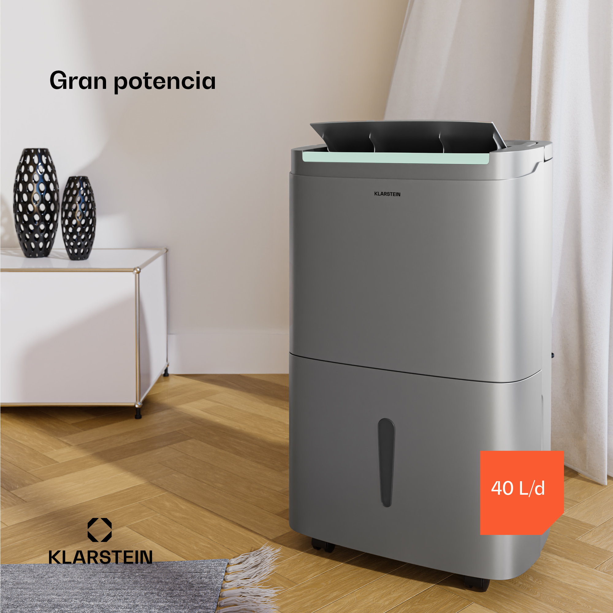 Un deumidificatore grigio è vicino a un mobile bianco e vasi. L'immagine ha un pavimento in legno e una tenda bianca.