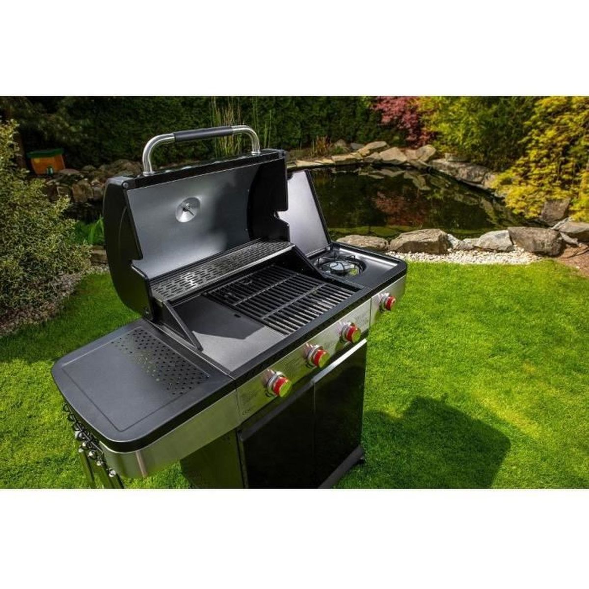 Ein offener Gasgrill in Schwarz und Silber steht auf einem grünen Rasen. Ein Teich und Grünzeug sind im Hintergrund.
