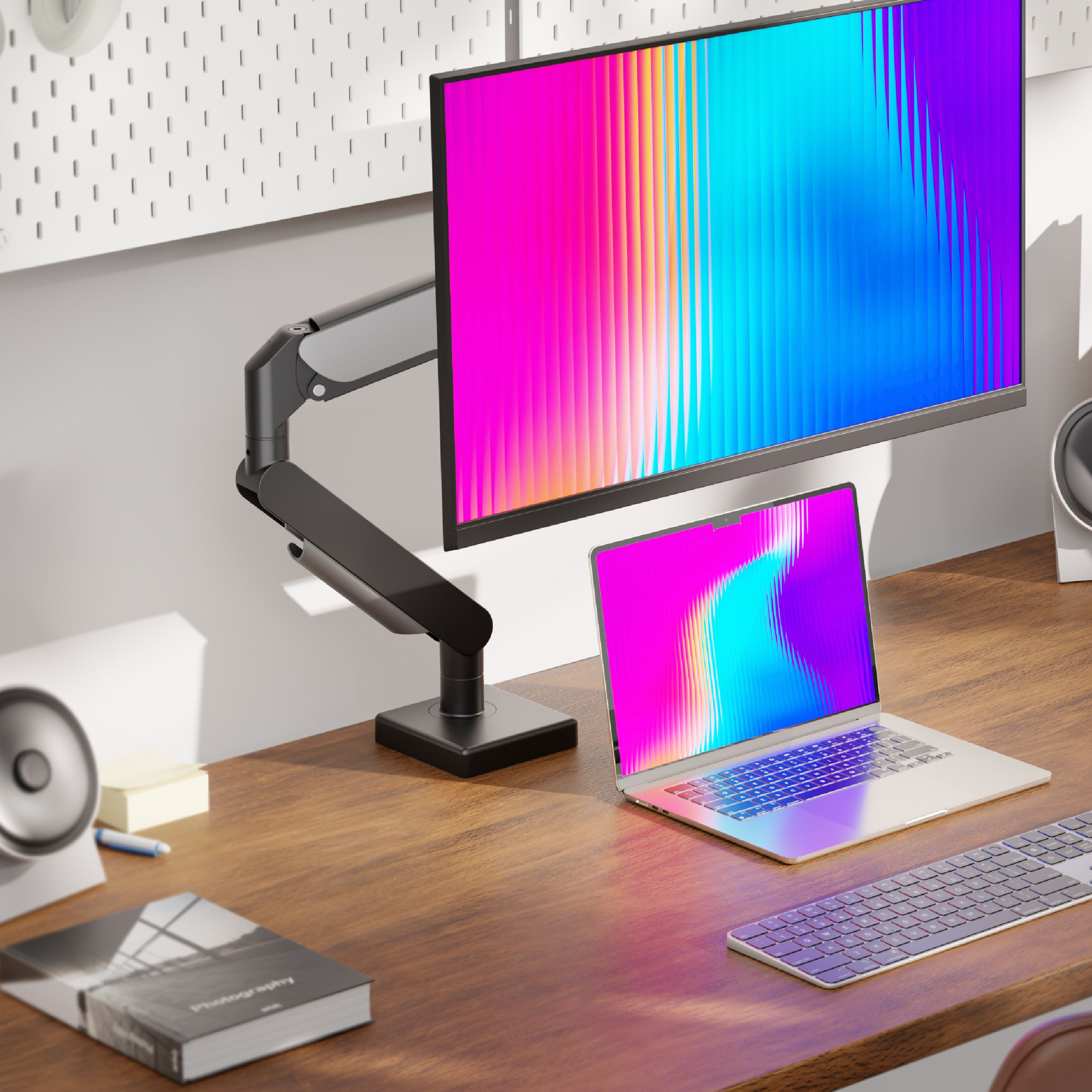 Konfiguracja biurka z monitorem, laptopem, klawiaturą i książką. Monitory i laptopy pokazują kolorowe gradienty.