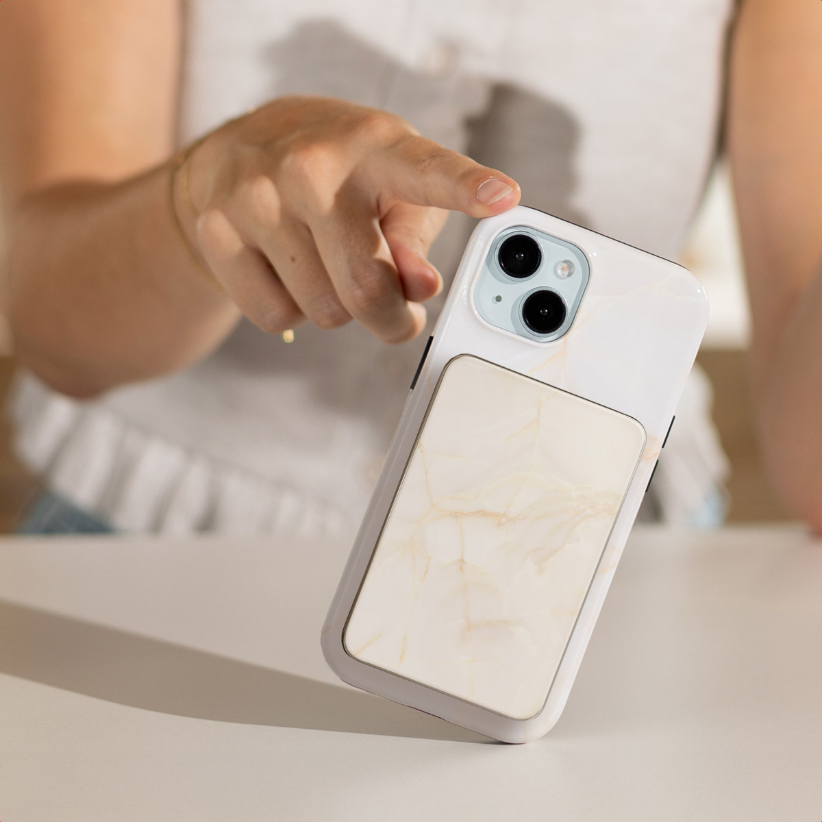 Een hand houdt een telefoon met marmerpatroon vast. De telefoon heeft een witte behuizing met een crème rechthoek.