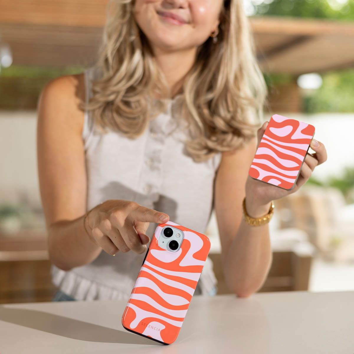 Vrouw die een telefoonhoesje en een kaart vasthoudt, beide met een oranje en roze wervelontwerp. De telefoon is zwart.