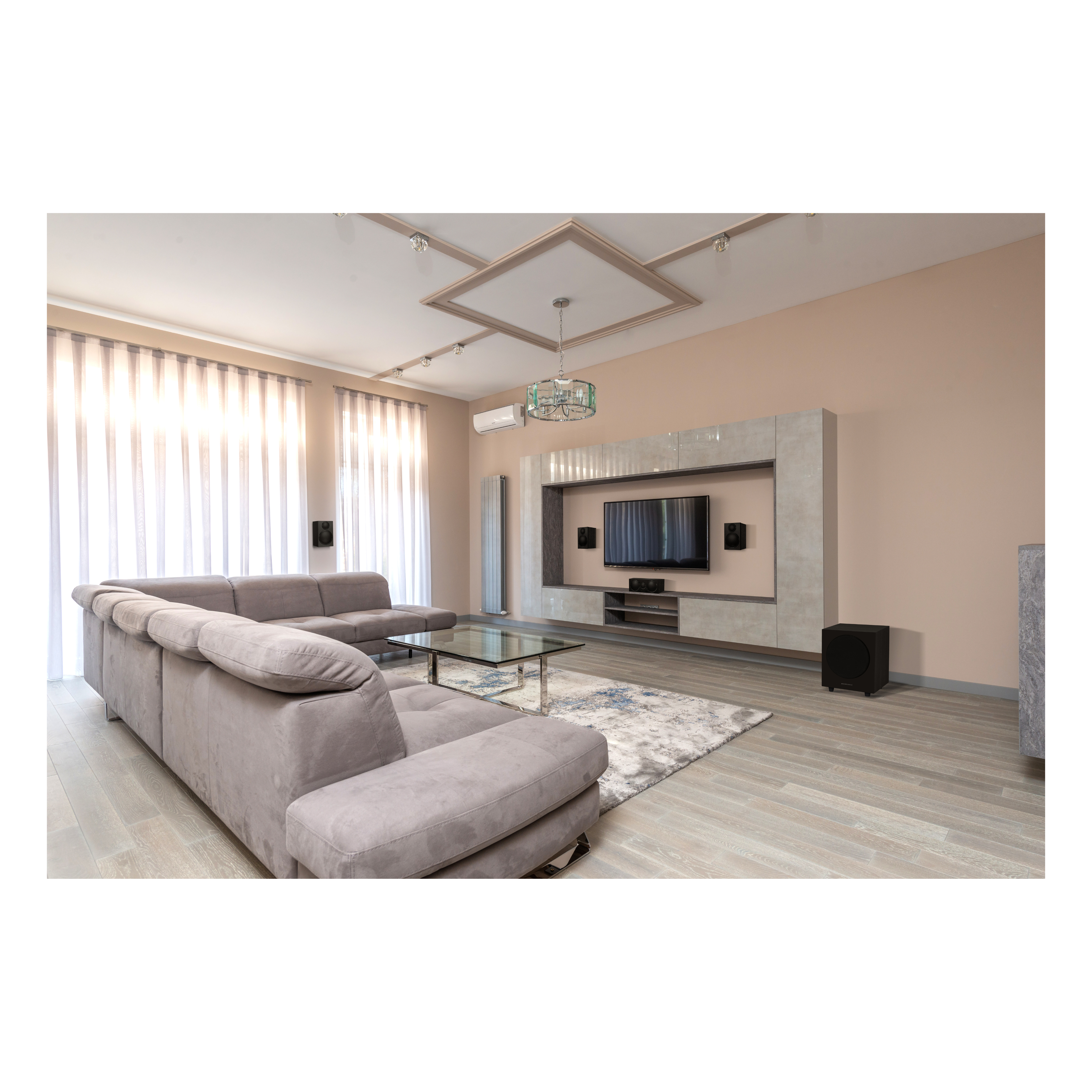 Woonkamer met grijze bank, tv, glazen tafel, vloerkleed en gordijnen. Lichtbeige muren en houten vloer. Kroonluchter.