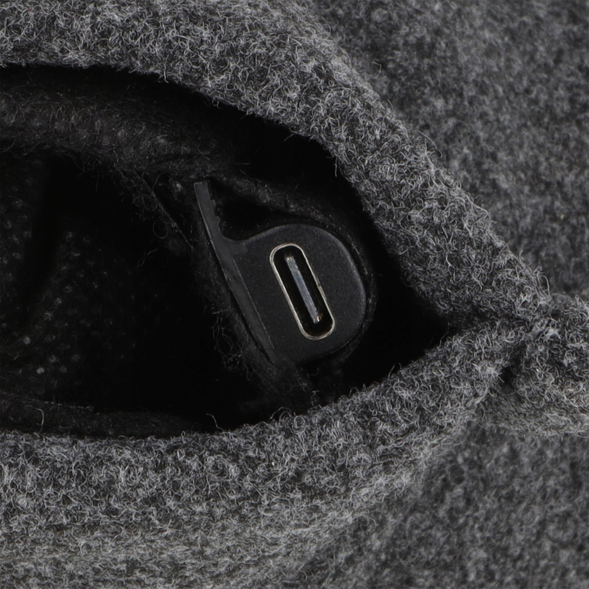 Zbliżenie szarej, teksturowanej tkaniny z widocznym czarnym portem USB-C. Port jest czarny ze srebrnym obramowaniem.