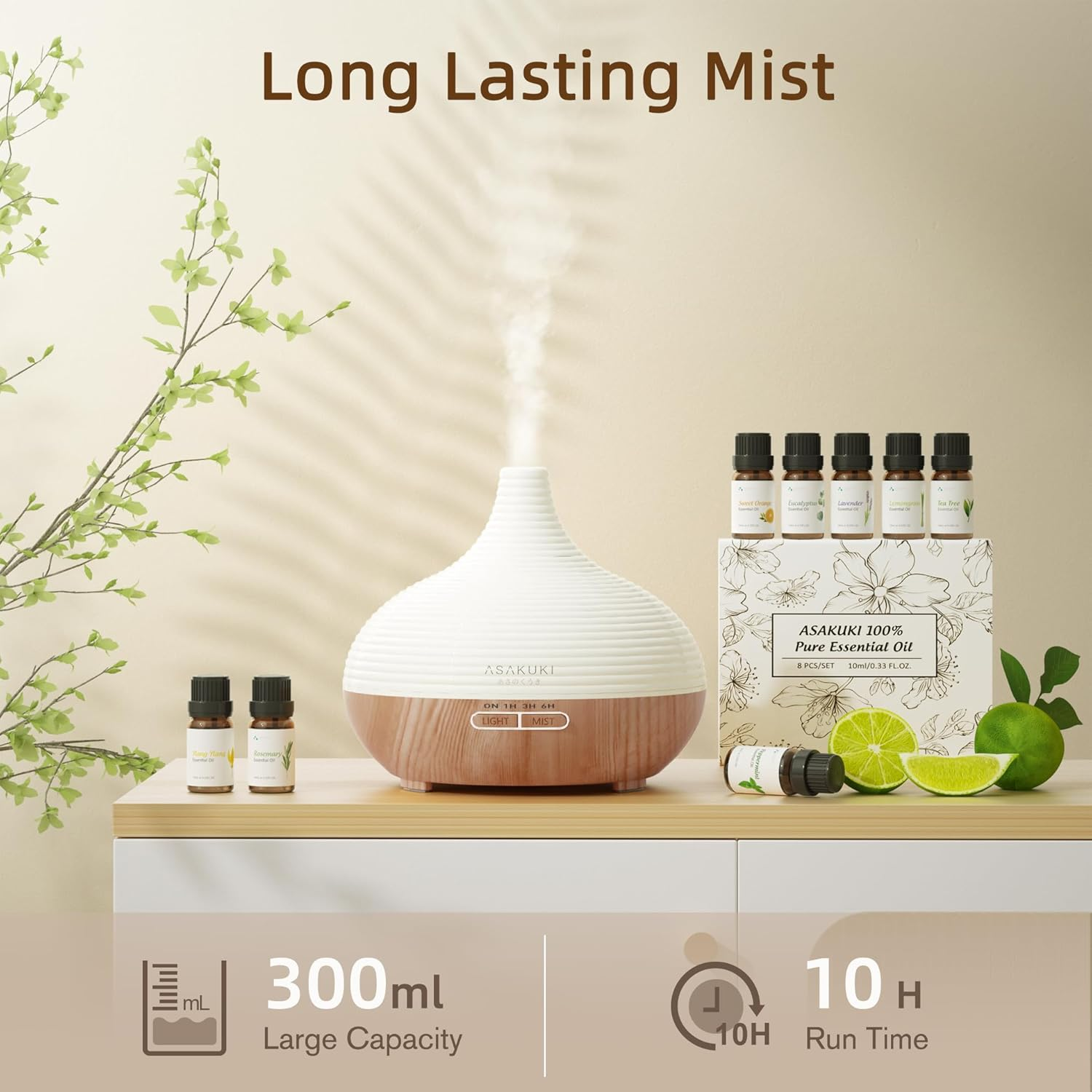 Ein Diffusor für ätherische Öle mit Nebel, Ölflaschen und Limetten auf einer weißen Oberfläche. Text: Long Lasting Mist, 300 ml und 10H Laufzeit.