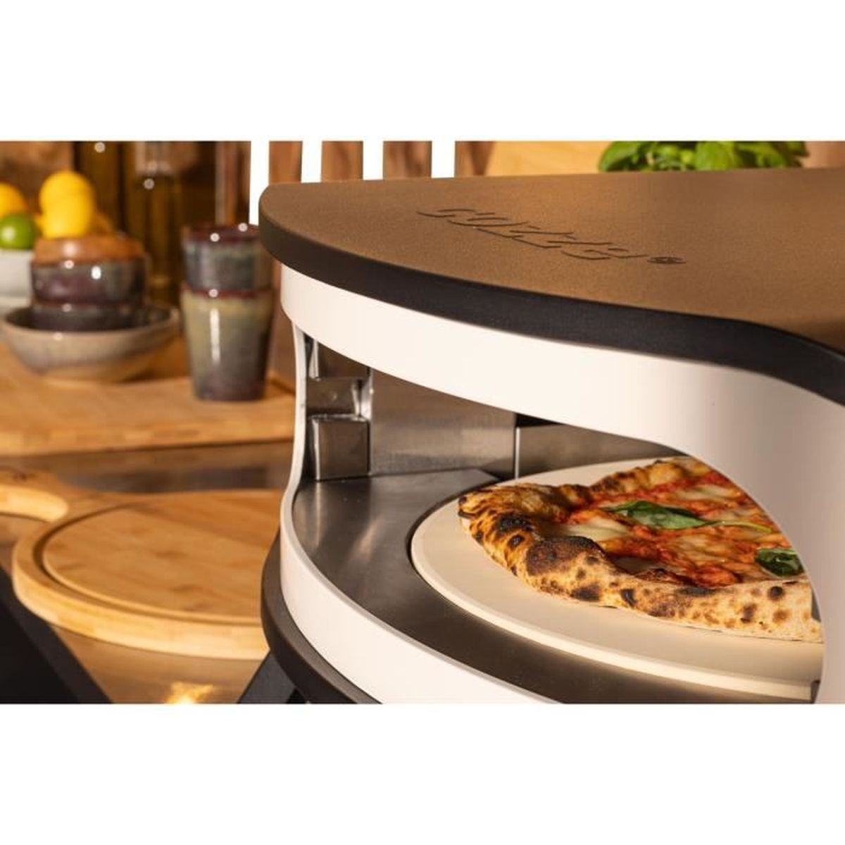 Een pizzaoven met een pizza erin. De oven is wit en bruin en heeft een pizza op een wit bord. Achtergrond heeft kommen en citroenen.