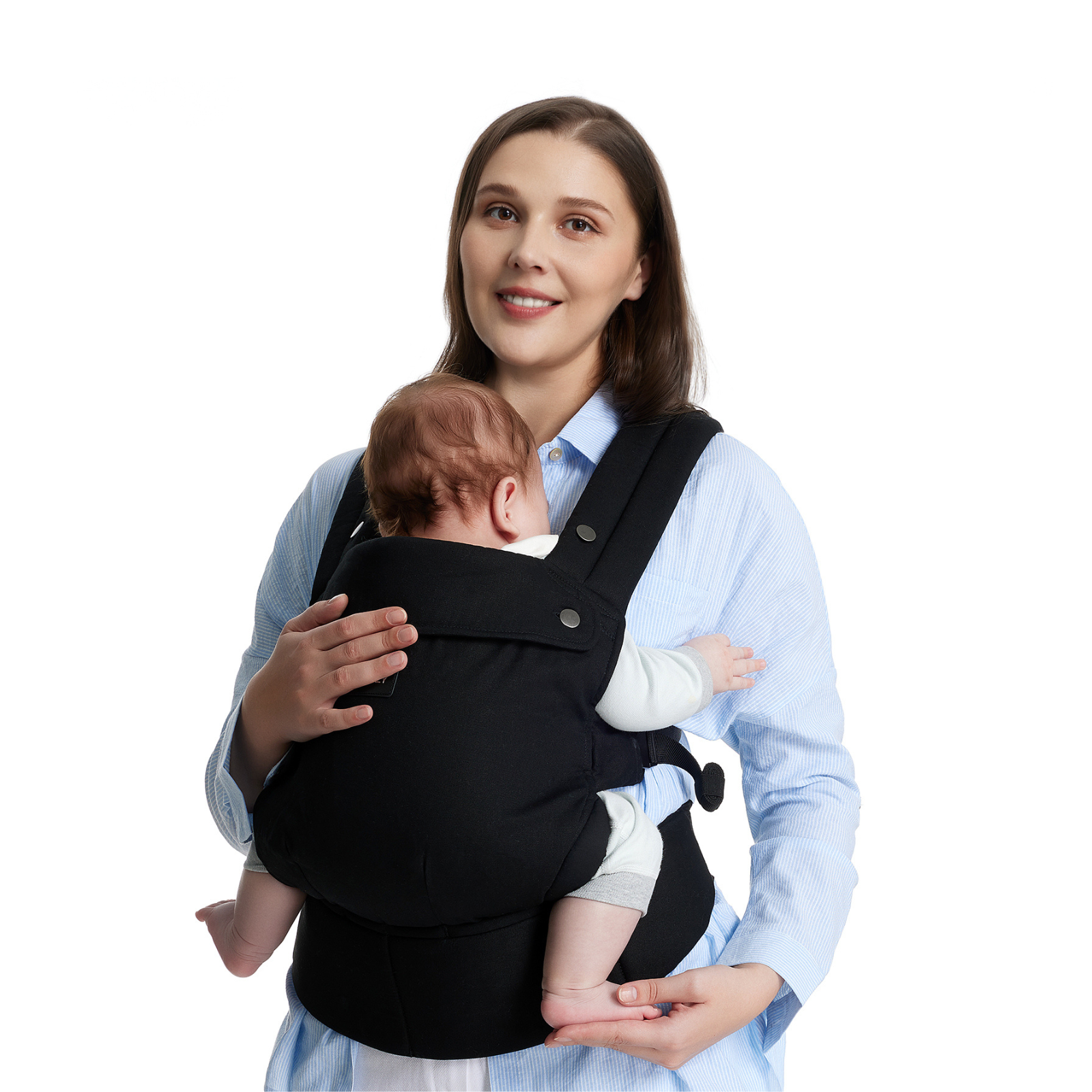 A woman holds a baby in a black baby carrier. The woman smiles. The background is white.