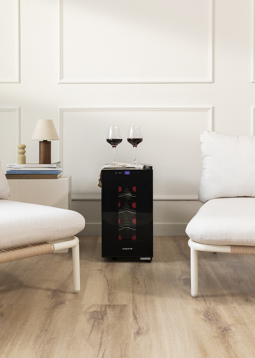 Un salón moderno con un enfriador de vino, dos copas de vino, dos sillones y una lámpara en una mesita auxiliar.