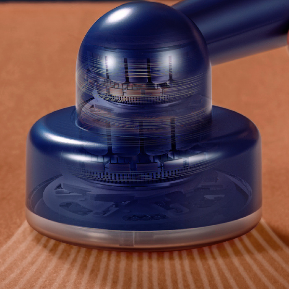Nahaufnahme eines blauen Geräts mit sichtbarer Innenmechanik. Es steht auf einer braunen, strukturierten Oberfläche. Das Gerät hat eine metallische Basis.