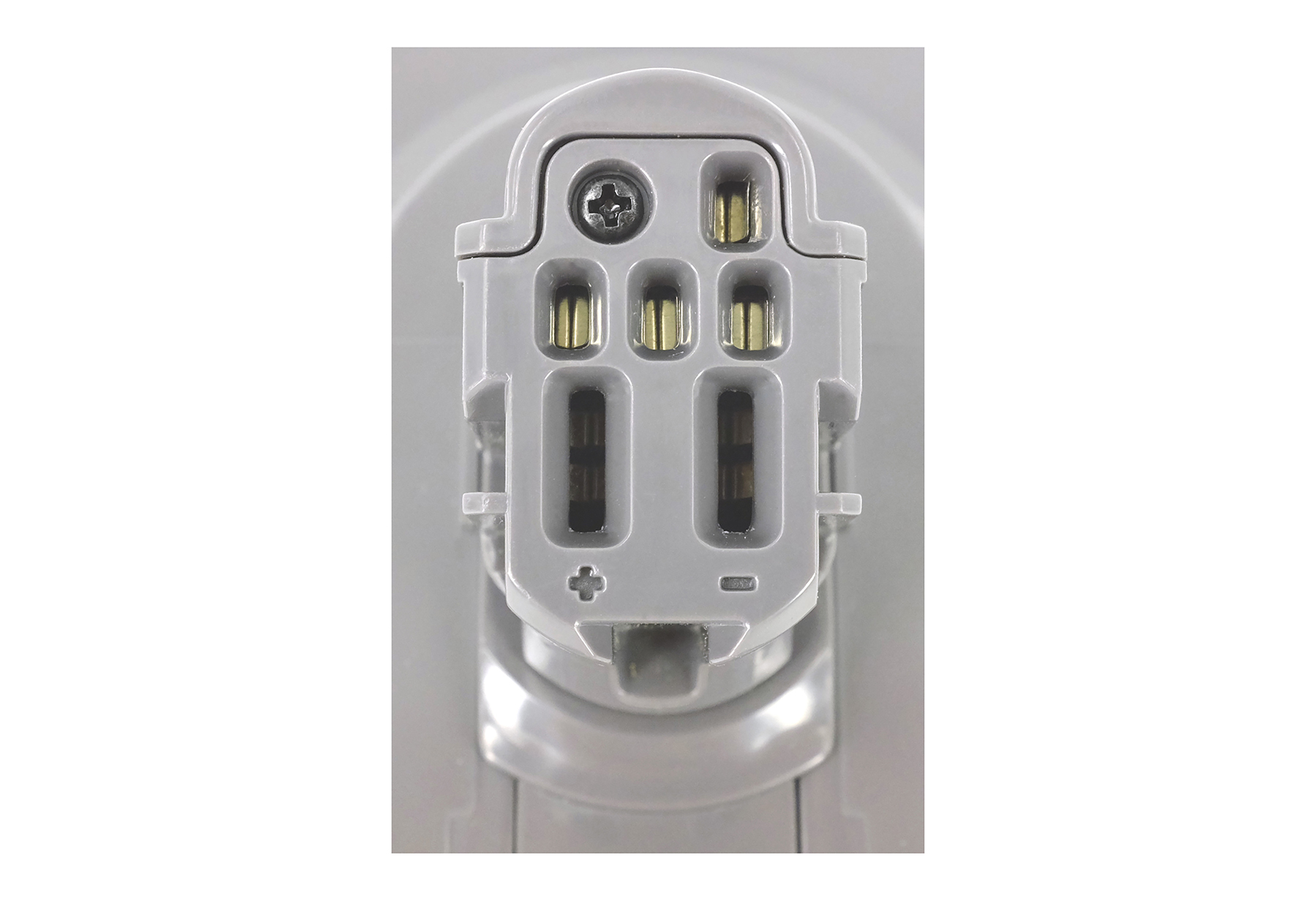 Nahaufnahme einer grauen elektronischen Komponente mit mehreren goldfarbenen Anschlüssen und einer Schraube. Die Komponente hat Schlitze und ein Plus/Minus-Zeichen.