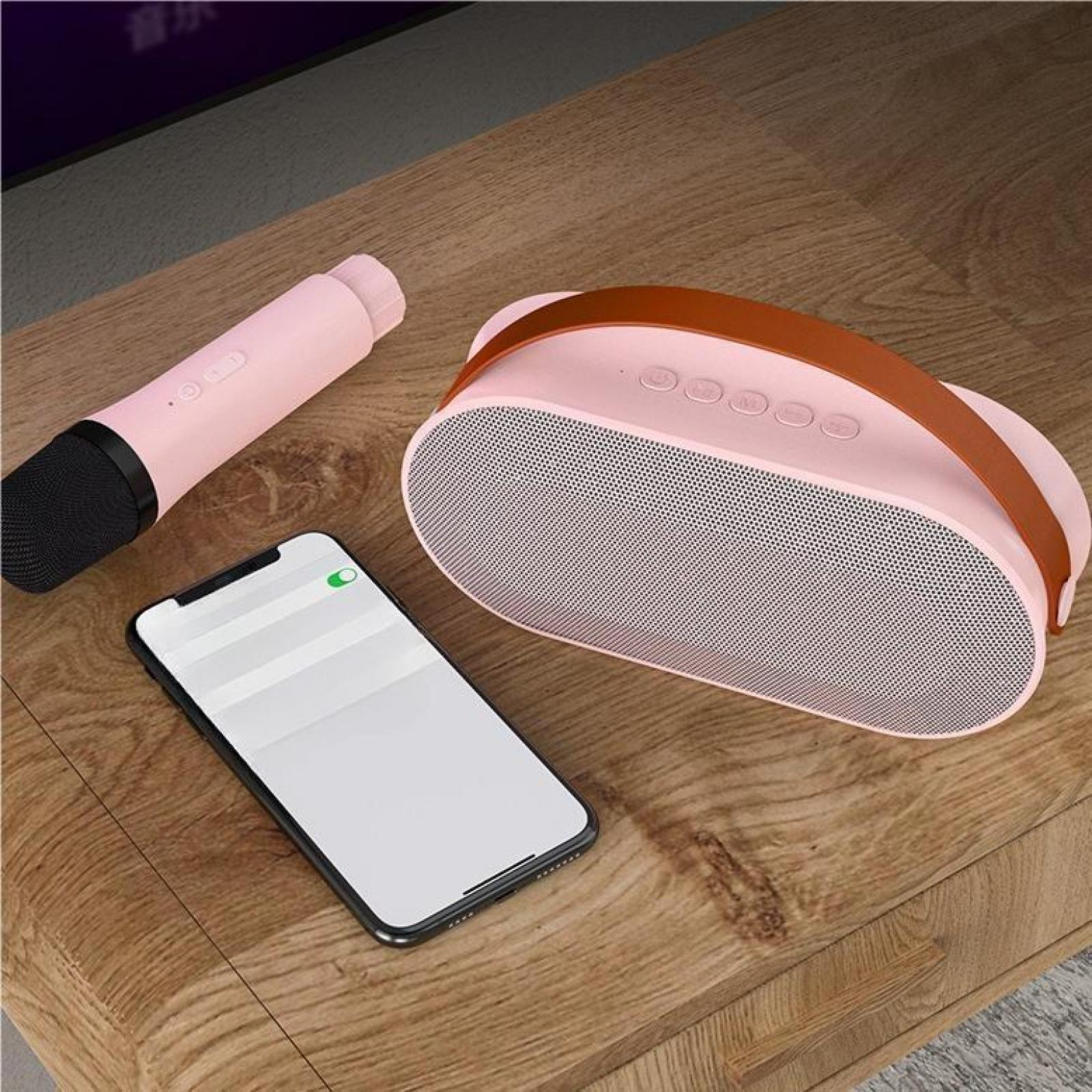 Ein rosa Lautsprecher, Mikrofon und Telefon liegen auf einer Holzoberfläche. Der Bildschirm des Telefons ist weiß und zeigt ein grünes Licht.