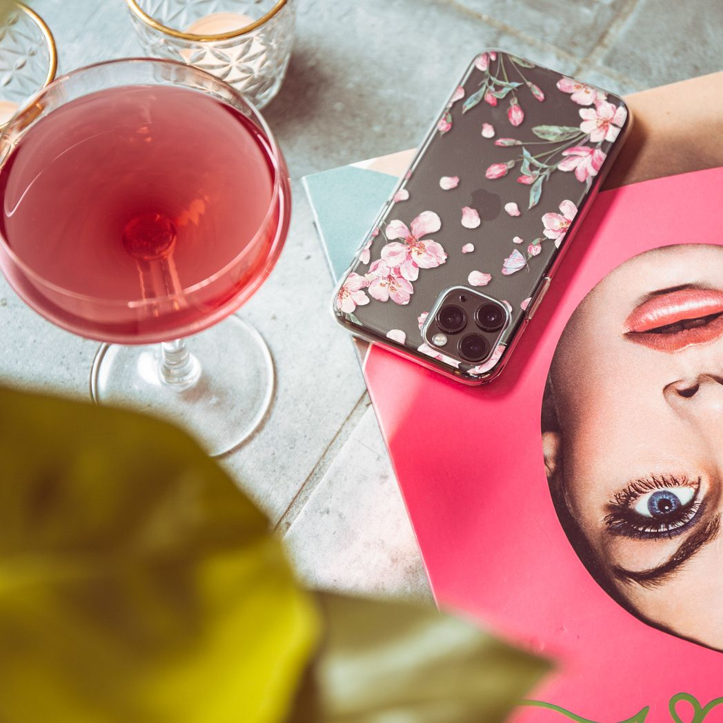 Un cocktail in un bicchiere, un telefono con custodia floreale e una rivista. La bevanda è rosa, la custodia ha fiori rosa.