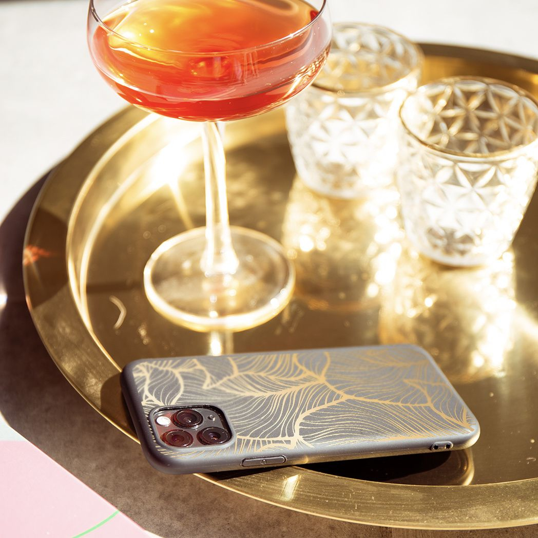 Een gouden dienblad met een cocktail, twee kaarsen en een telefoon met een gouden bladontwerp. De scène wordt door zonlicht verlicht.