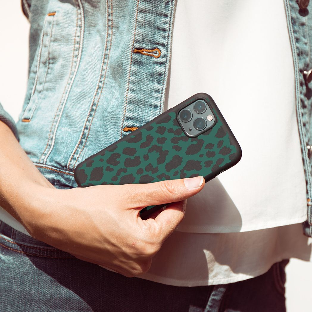 Una persona tiene in mano un telefono con una custodia con stampa leopardata verde. La persona indossa una giacca di jeans e una camicia bianca.