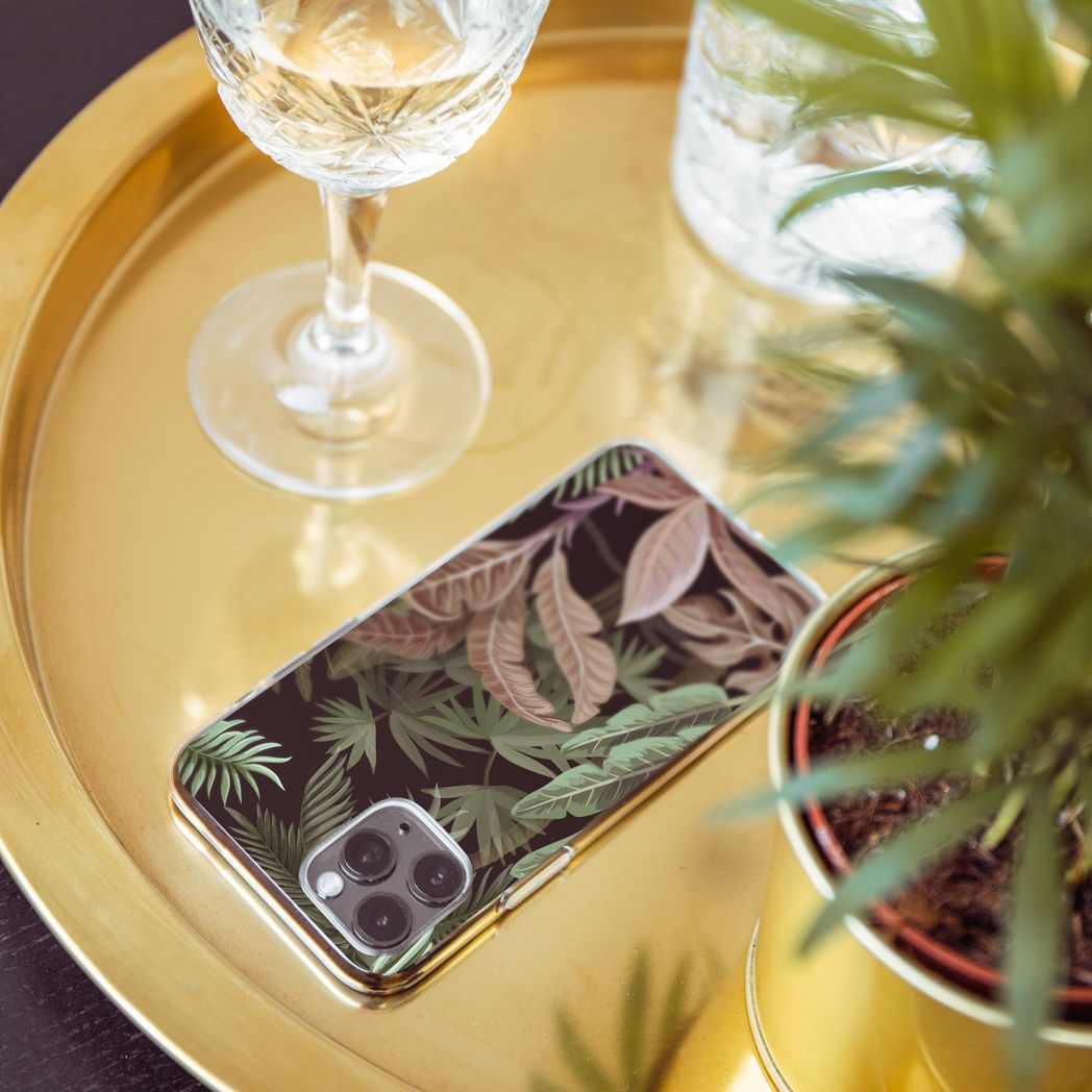 Un vassoio dorato contiene un telefono con motivo a foglie, un bicchiere da vino, un bicchiere d'acqua e una piccola pianta in vaso.