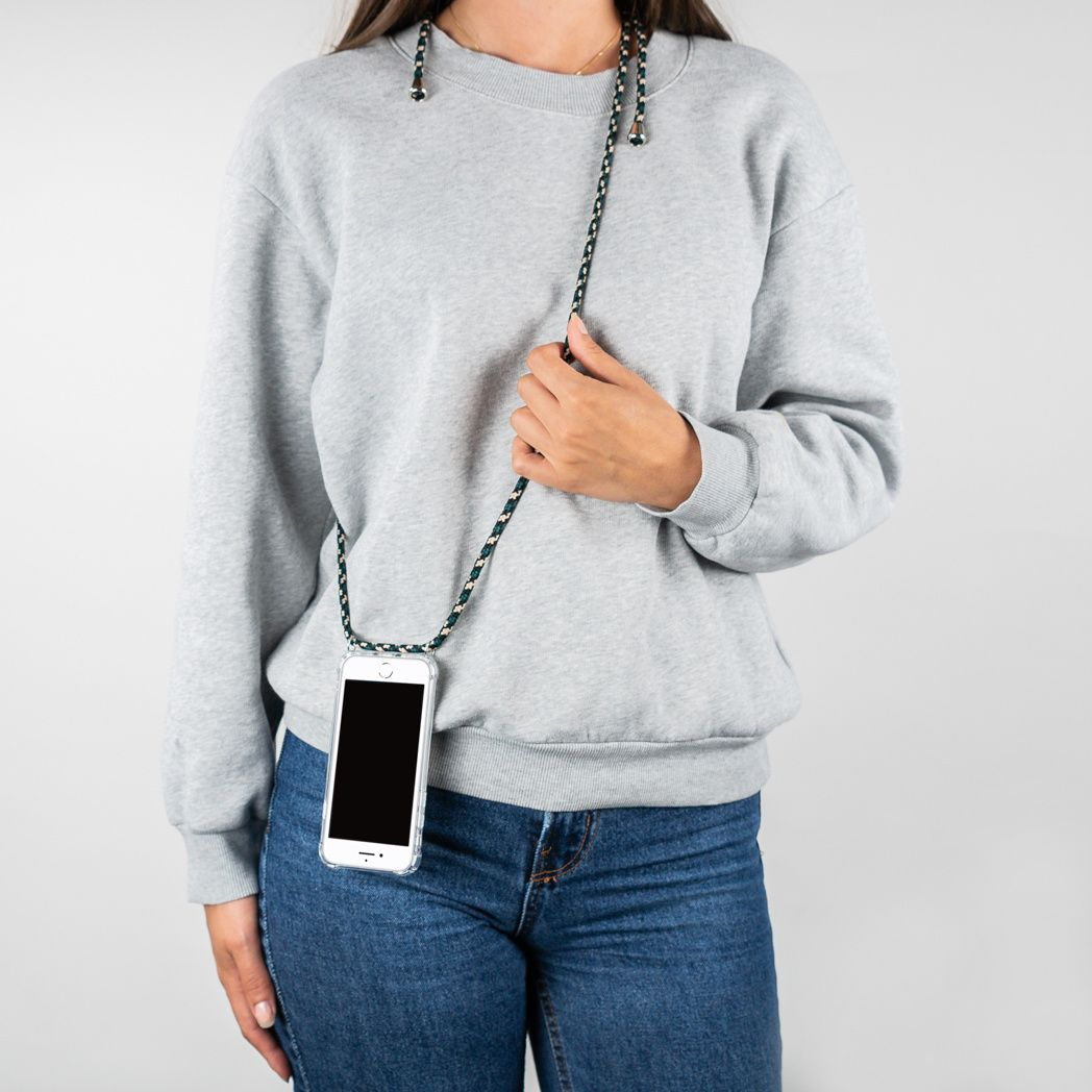 Een persoon met een grijze trui en een blauwe spijkerbroek houdt een telefoon vast met een koord. De telefoon zit in een doorzichtig hoesje.