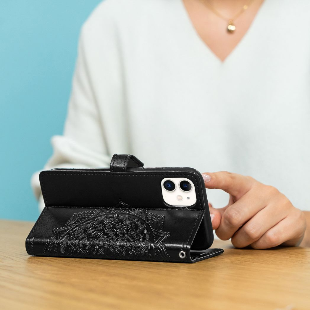 Una persona tiene in mano un telefono nero in una custodia nera con un disegno in rilievo. Il telefono poggia su un tavolo di legno.