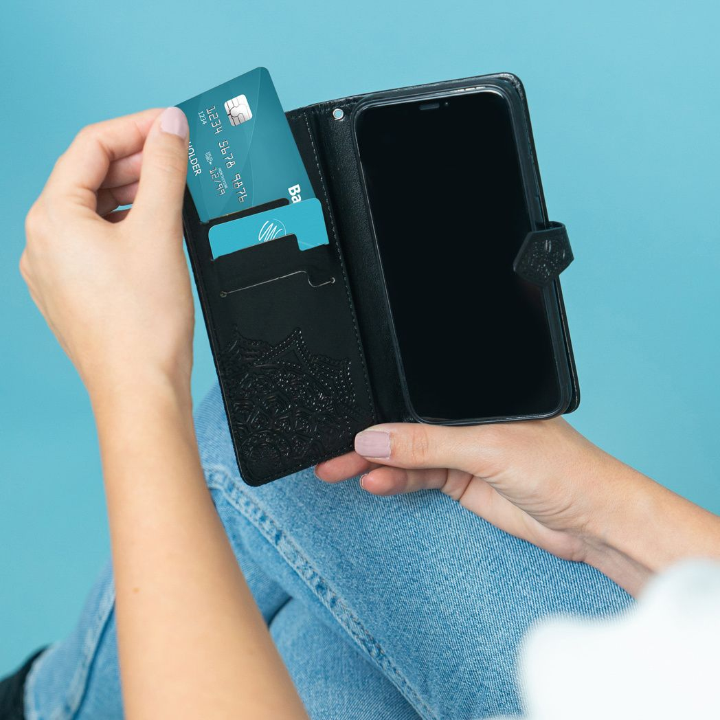 Una persona tiene in mano una custodia nera per telefono con un telefono e carte di credito. Lo sfondo è azzurro.