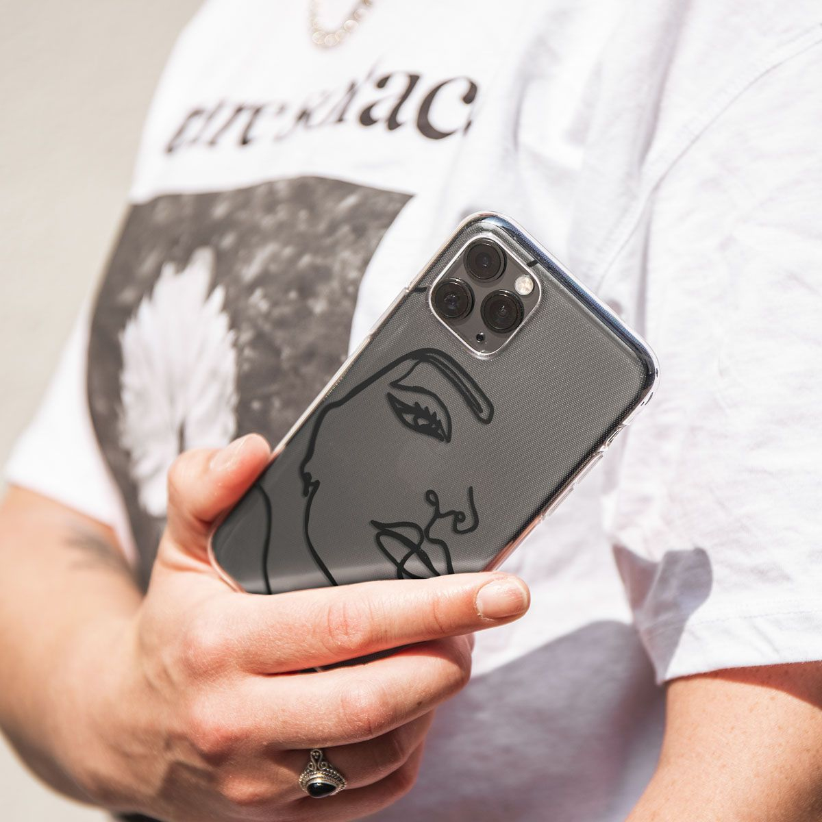 Een persoon houdt een telefoon met een gezichtsontwerp vast. De persoon draagt een wit t-shirt. De telefoonhoes heeft een zwart lijngezicht.