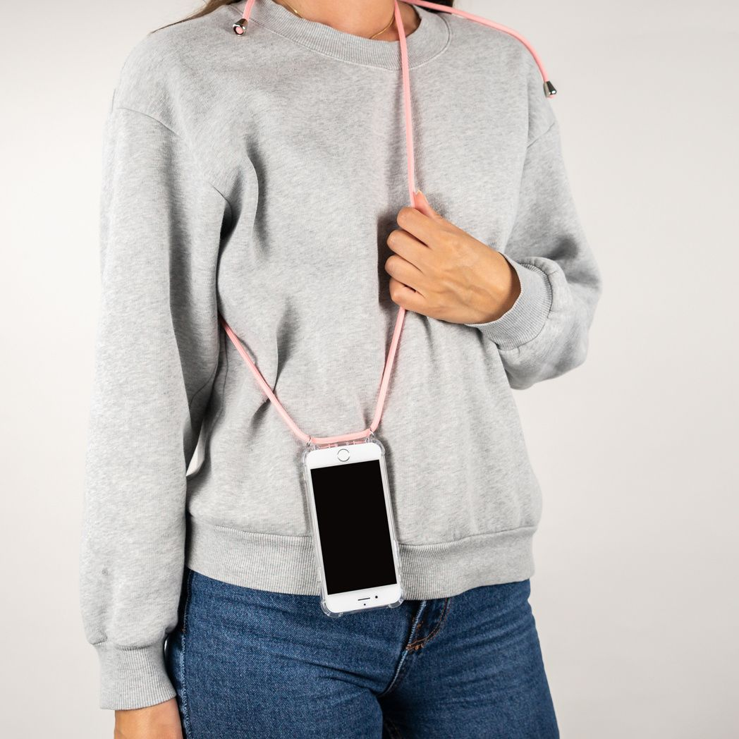 Een persoon in een grijze trui en een blauwe spijkerbroek houdt een telefoon vast met een roze koord. De telefoon zit in een doorzichtig hoesje.