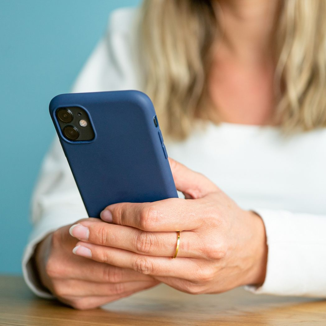 Une femme tient un smartphone bleu. Elle porte un haut blanc et une bague dorée. Le fond est bleu clair.