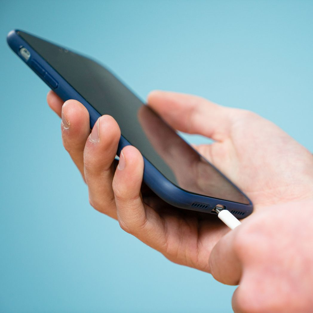 Une main tient un téléphone bleu, connectant un câble de charge blanc. L'arrière-plan est bleu clair.